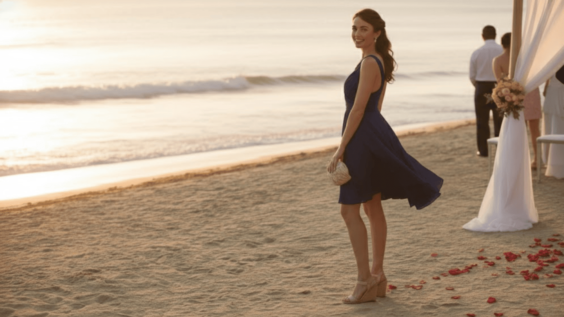 a woman wearing a knee-length navy blue cocktail dress with wedge sandals, standing on a beach wedding venue