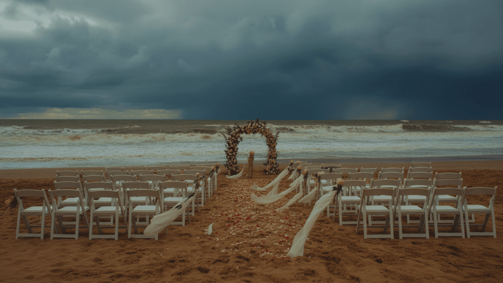 stormy and windy weather on a beach with wedding decorations including chairs, an arch, flowers, and flowing fabric