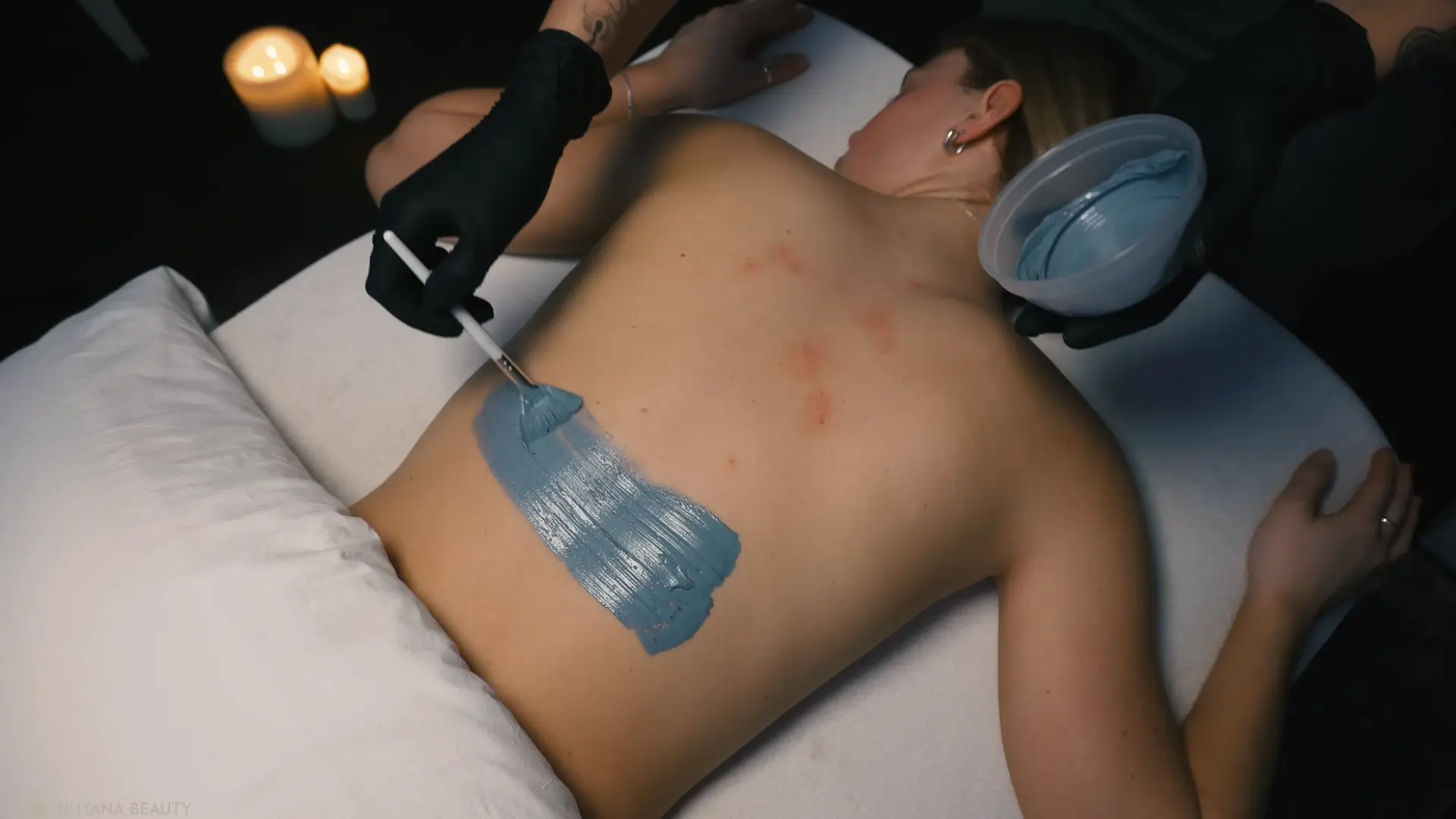 applying a charcoal bamboo treatment to the back during the facial, with the product being gently spread in circular motions