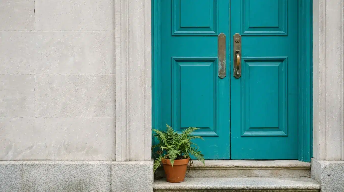 Teal double doors with brass handles and potted fern on stone doorstep