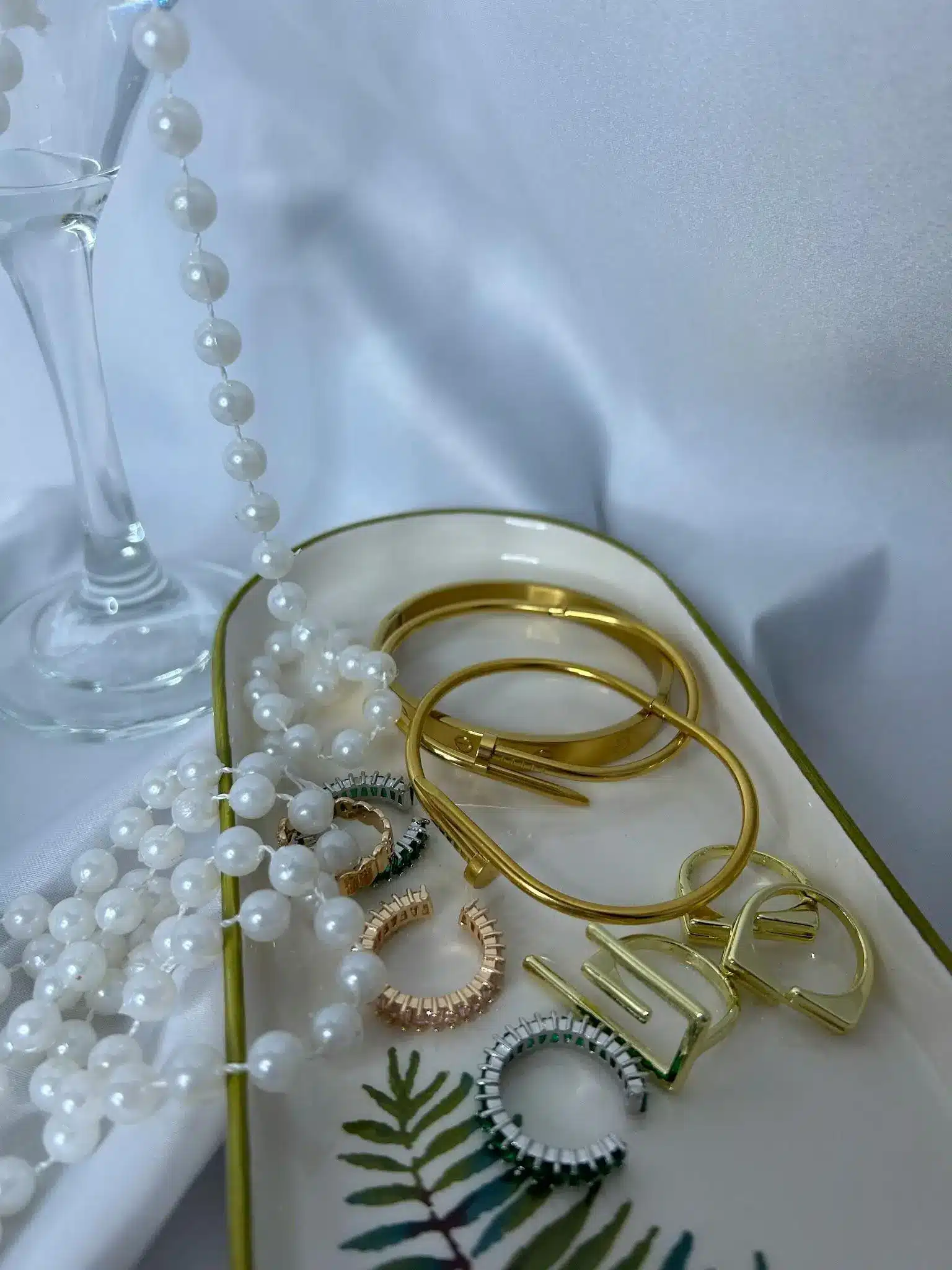 Gold jewelry and pearl necklace on decorative ceramic tray with leaf design
