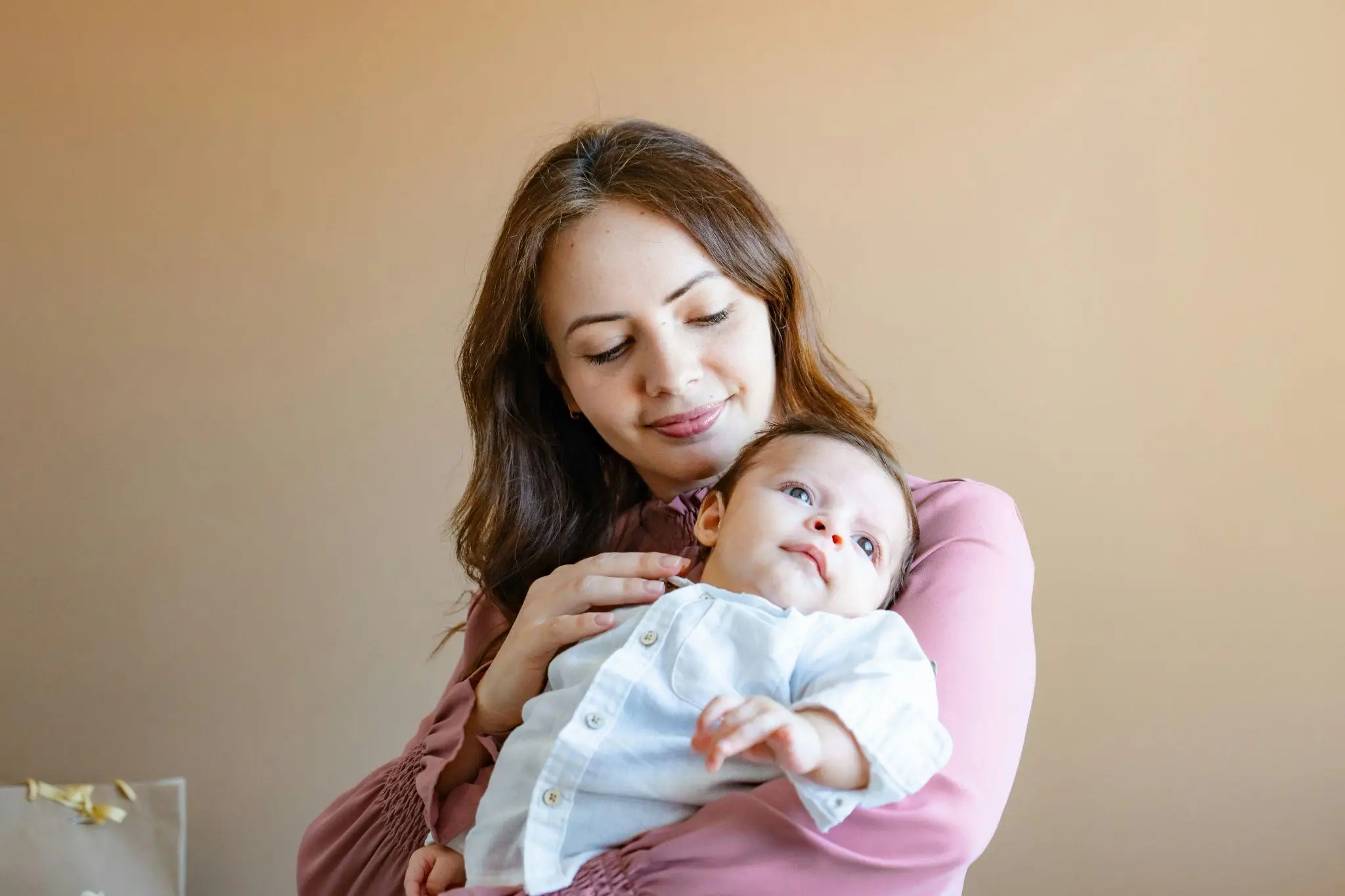 Mother holding baby in cozy room with warm lighting and beige wall background