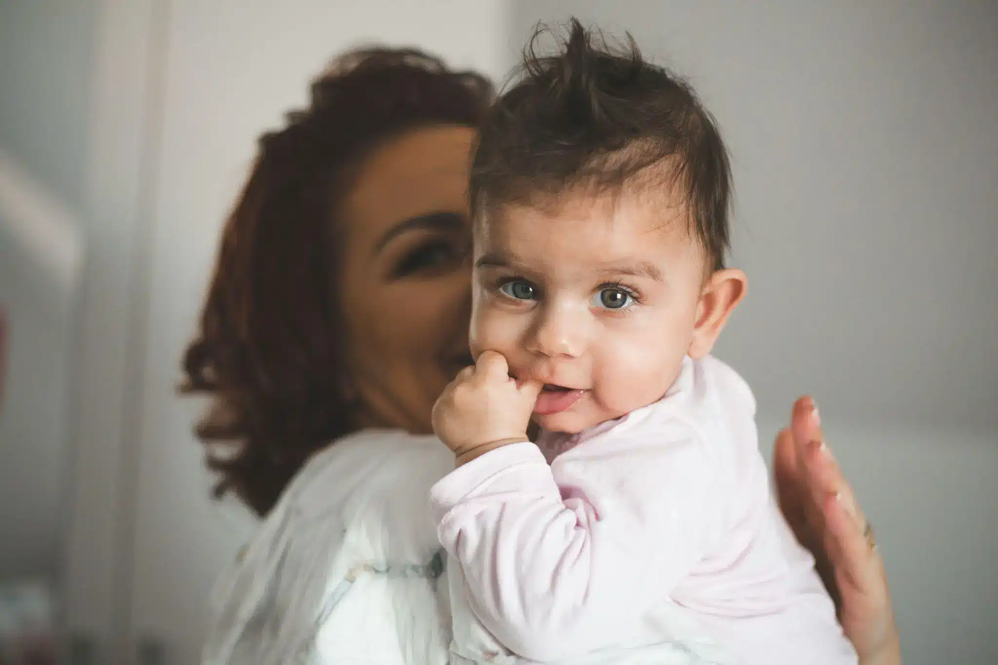 Baby in pink outfit resting on woman's shoulder in soft-lit indoor setting