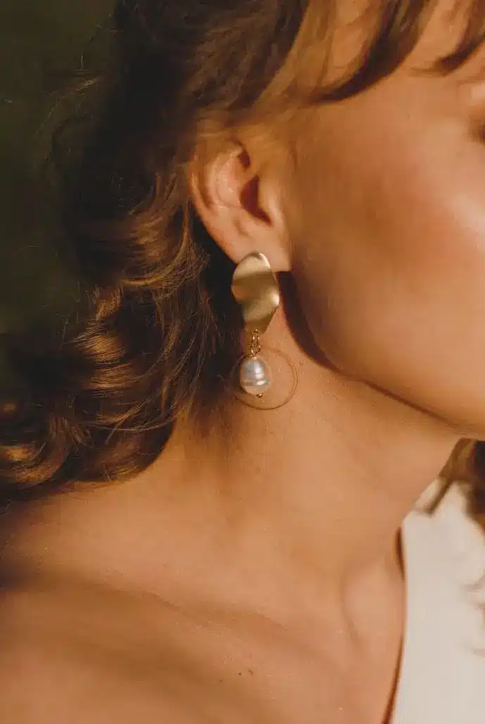 Gold earring with pearl detail worn by woman in warm natural light