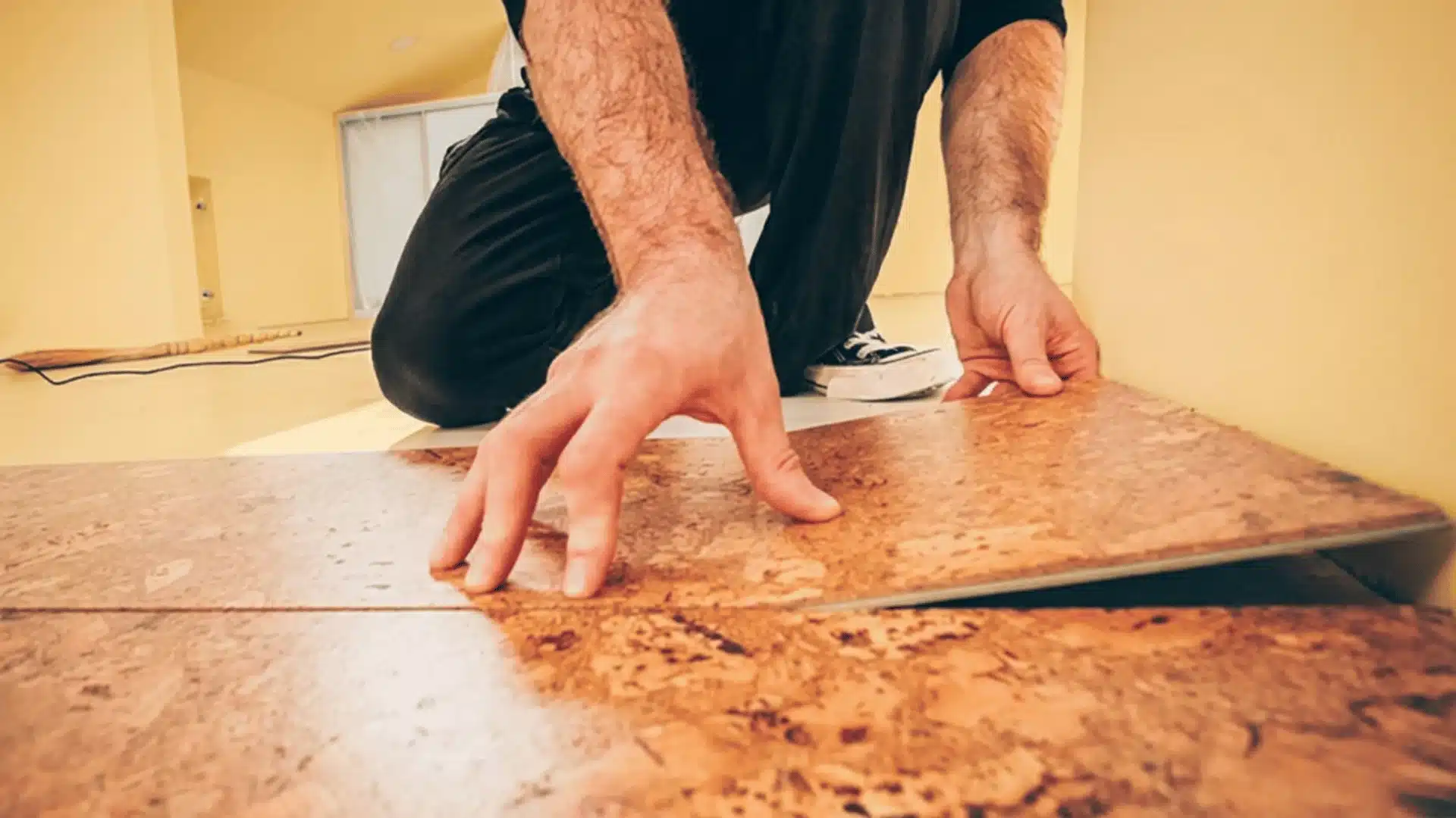 the picture show a man placing flooring in black dress and butter yellow back ground