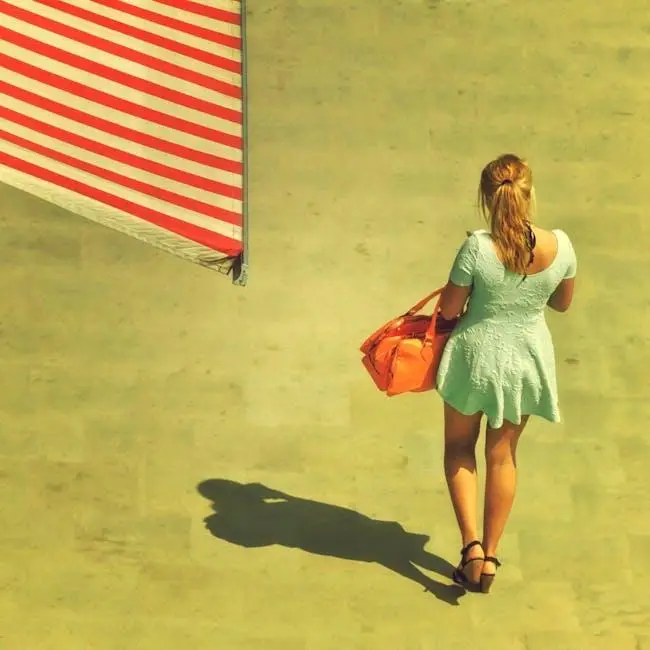 Woman in blue dress carrying orange bag, walking on sunny pavement near American flag
