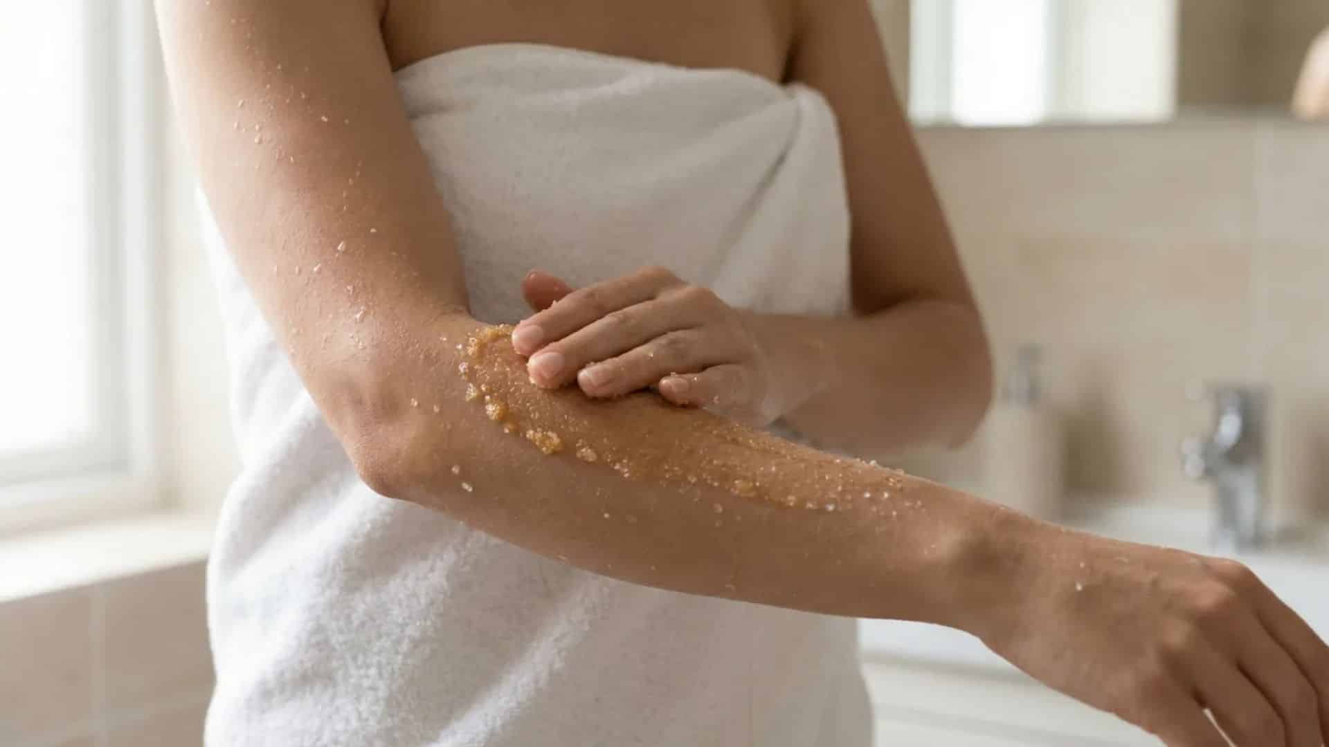 woman in towel exfoliating her forearm with grainy scrub, close-up on arm, face not visible