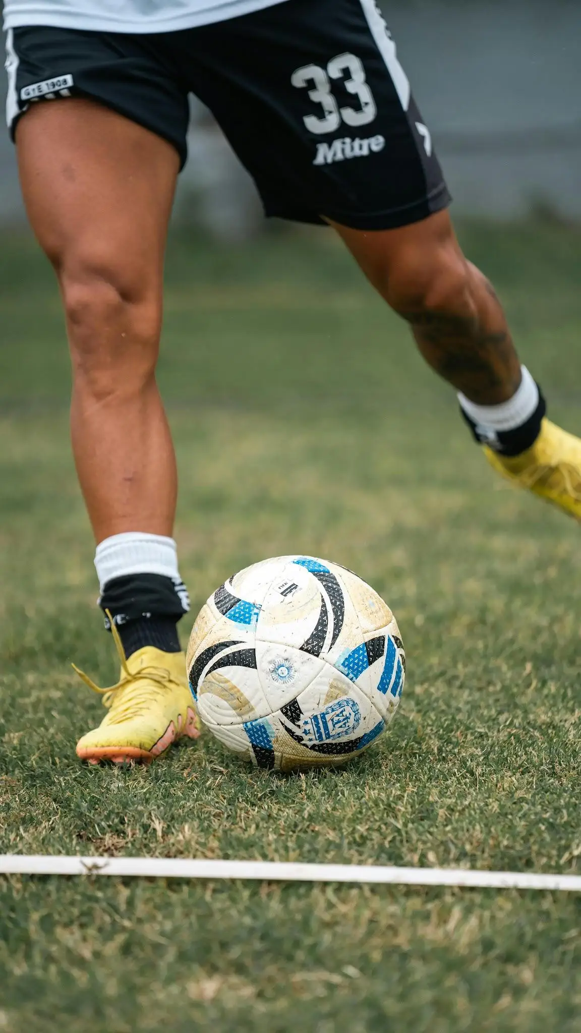 Soccer player with yellow cleats about to kick a ball on grassy field