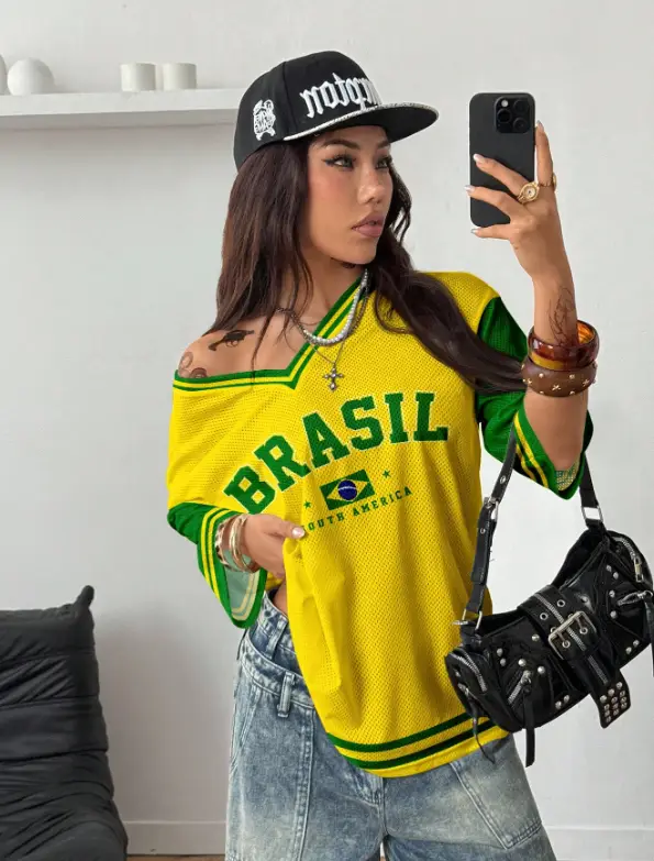 Woman in yellow Brazil jersey taking a selfie in modern room with black cap and bag