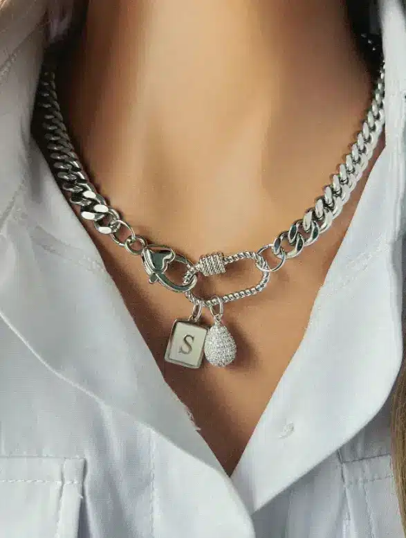 Silver chain necklace with charms over white collared shirt in close-up view