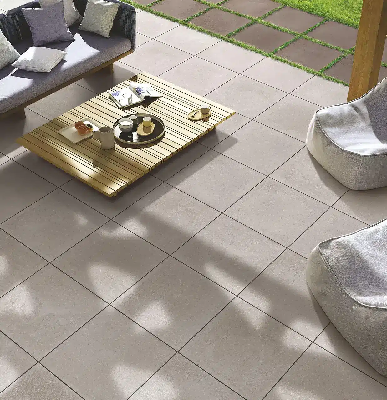 Modern outdoor patio with beige tiled floor, wooden coffee table, and cushioned seating in sunlight