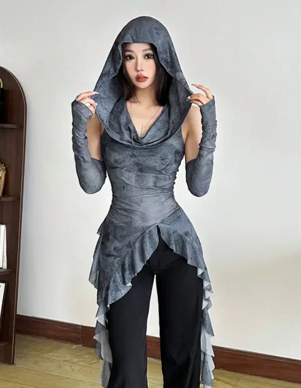 Woman in a gray hooded outfit with ruffled hem standing indoors