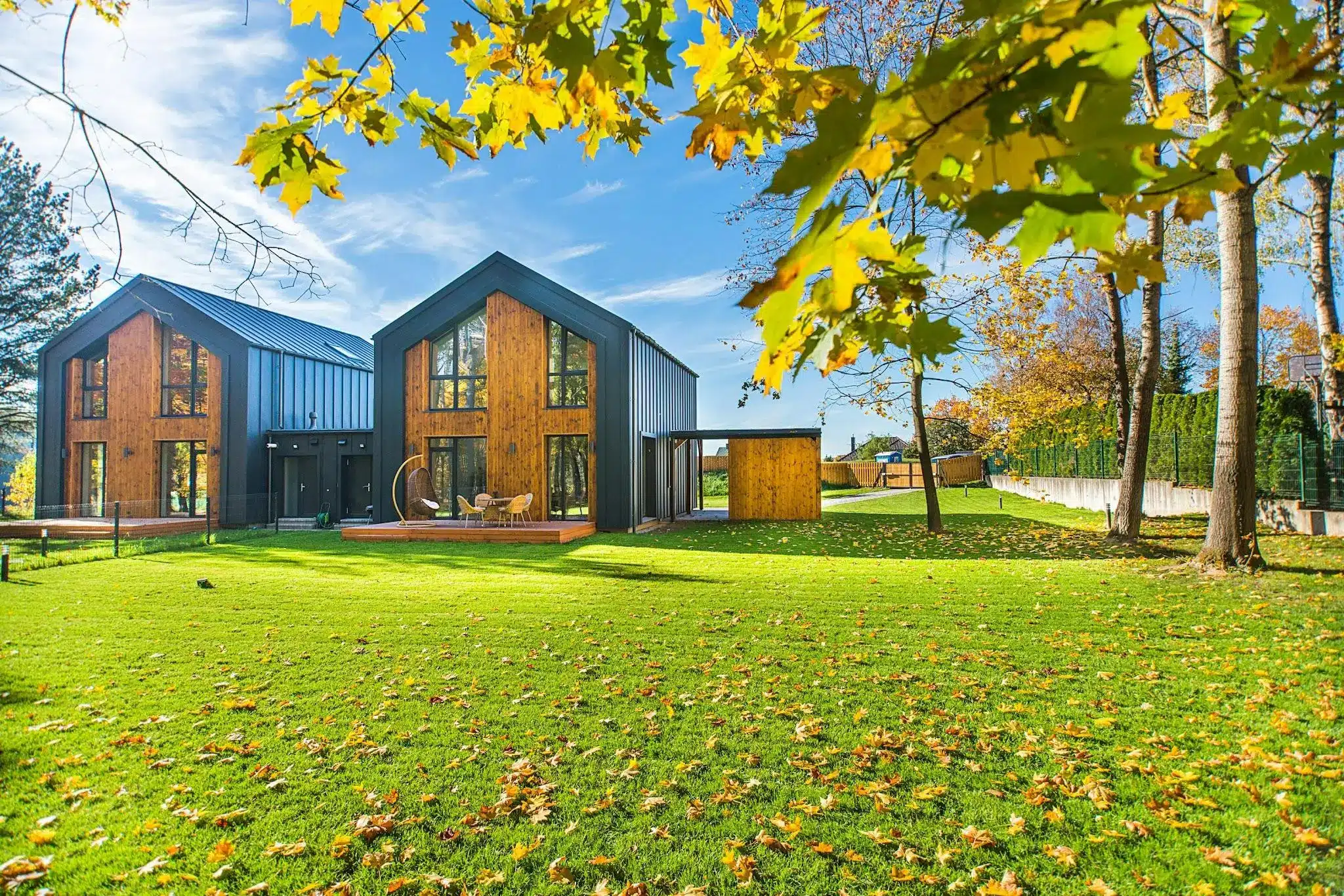 Modern wooden houses with large windows on lush green lawn in autumn setting