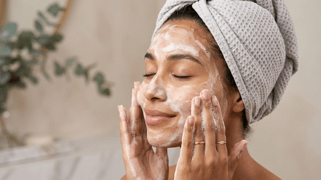 Woman gently cleansing face with foaming cleanser, wearing a towel wrap, focused on skincare routine at home