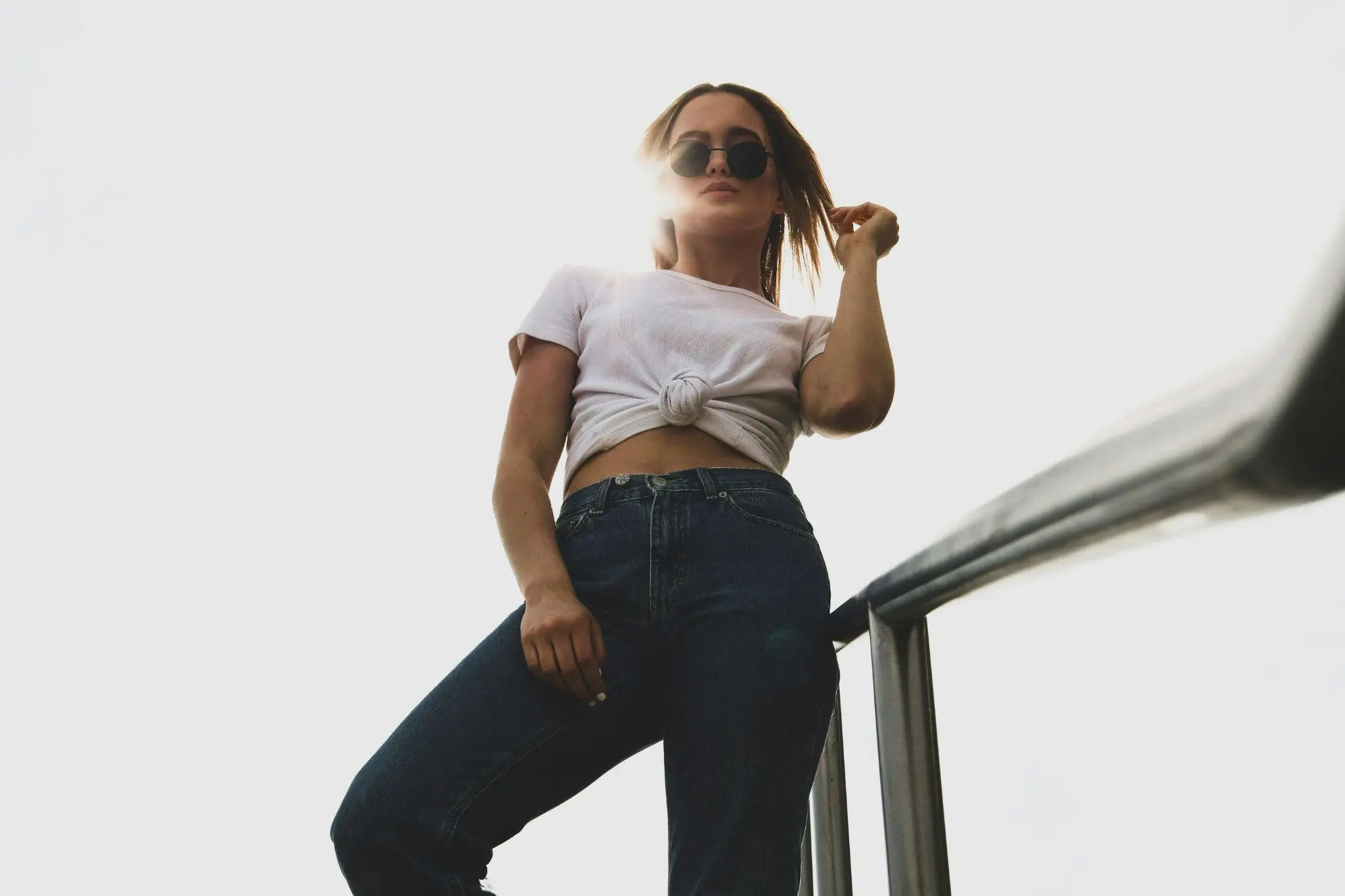 Person wearing sunglasses and white shirt, standing outside against bright sky.