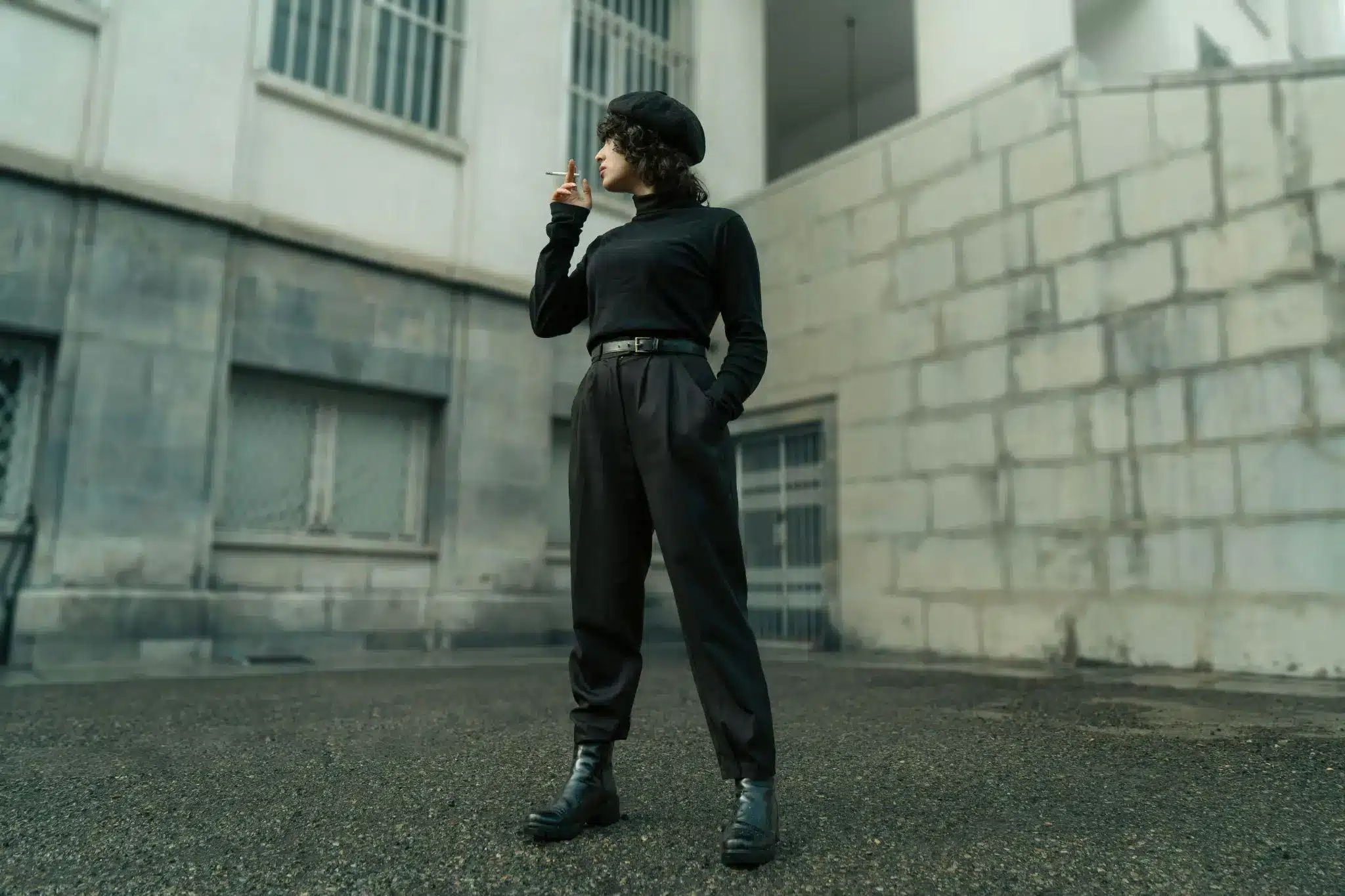 Person in black outfit smoking outside against urban stone building backdrop