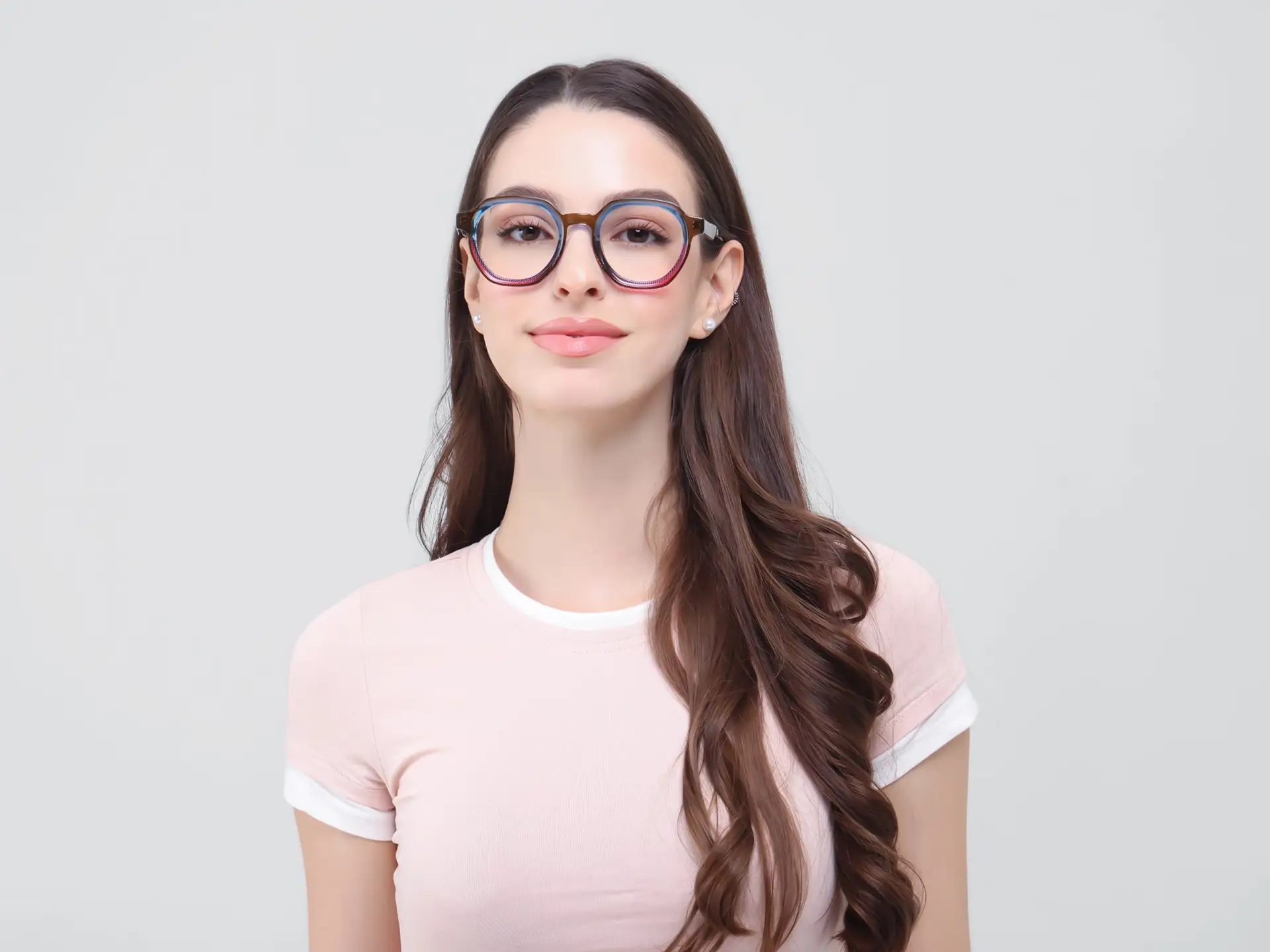 Young woman with glasses and long brown hair wearing a pink shirt against a gray background