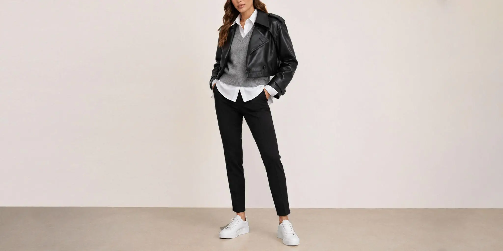 Person wearing black leather jacket, gray sweater, and white sneakers in minimalist indoor setting