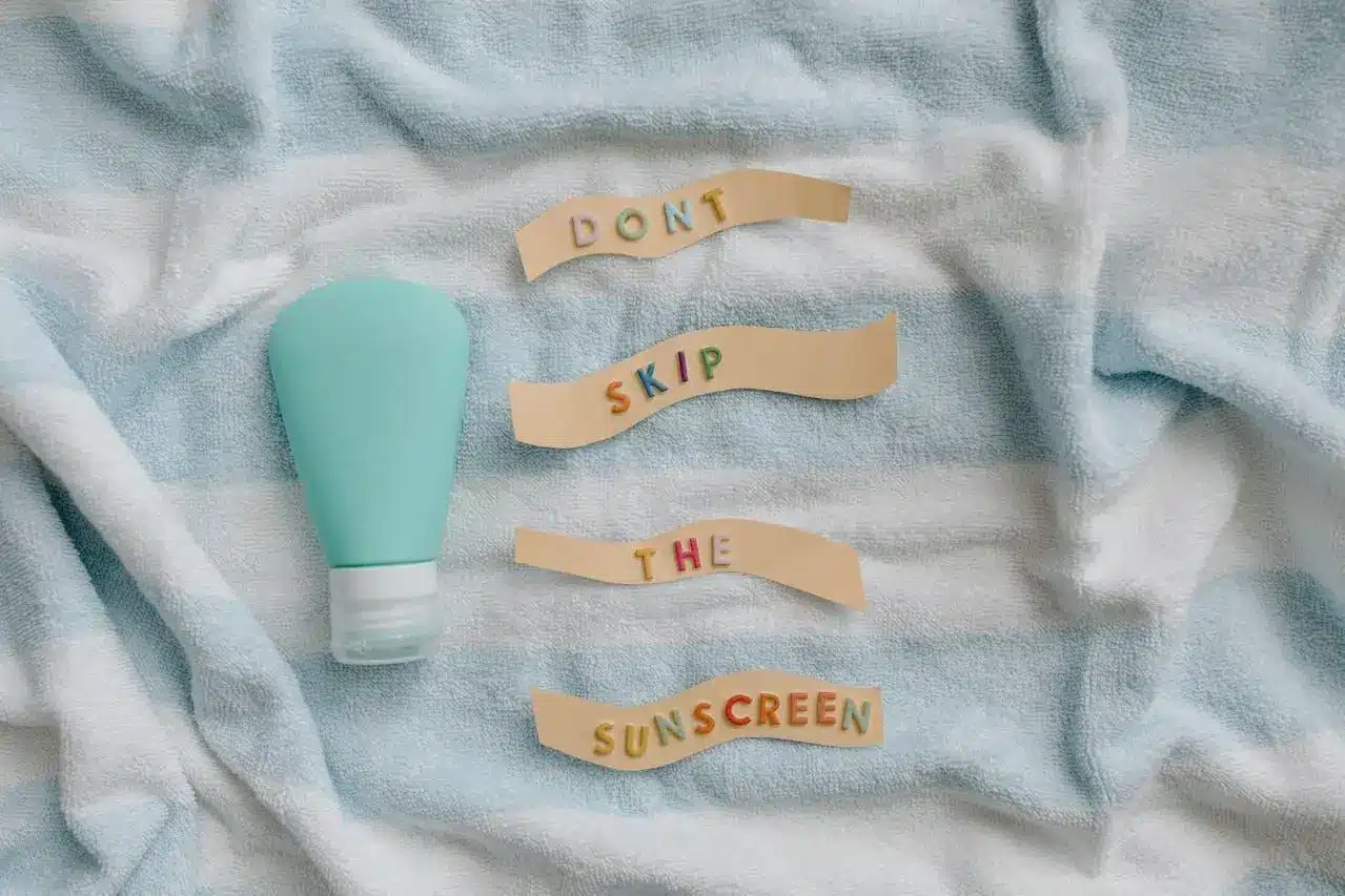 Teal sunscreen bottle on striped towel with pastel letters spelling message