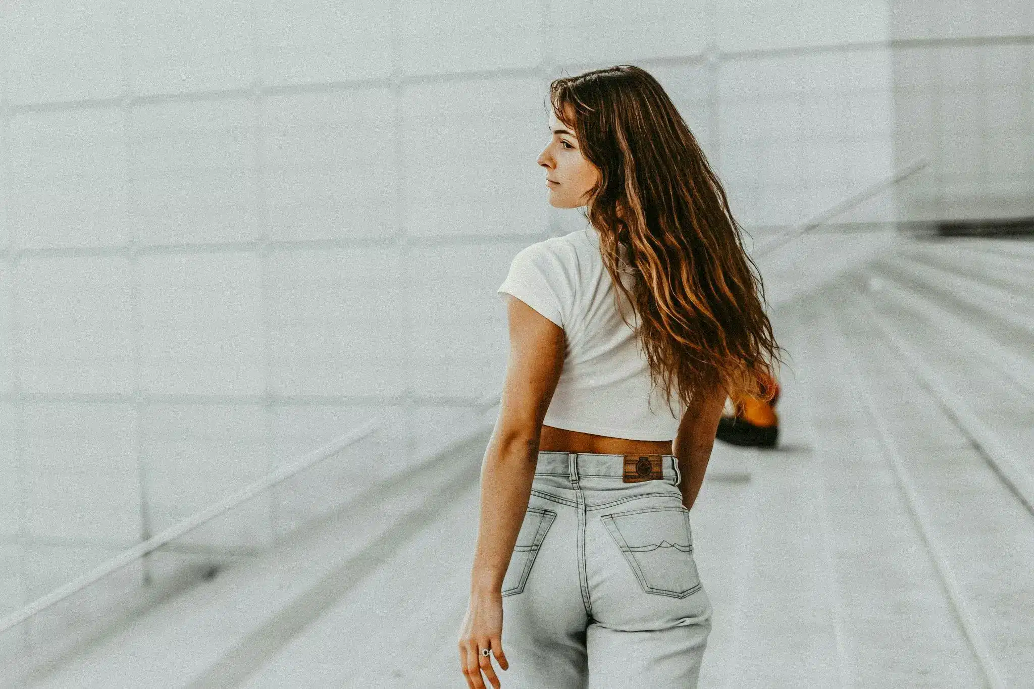 Woman with long hair in white top and jeans standing on gray stairs