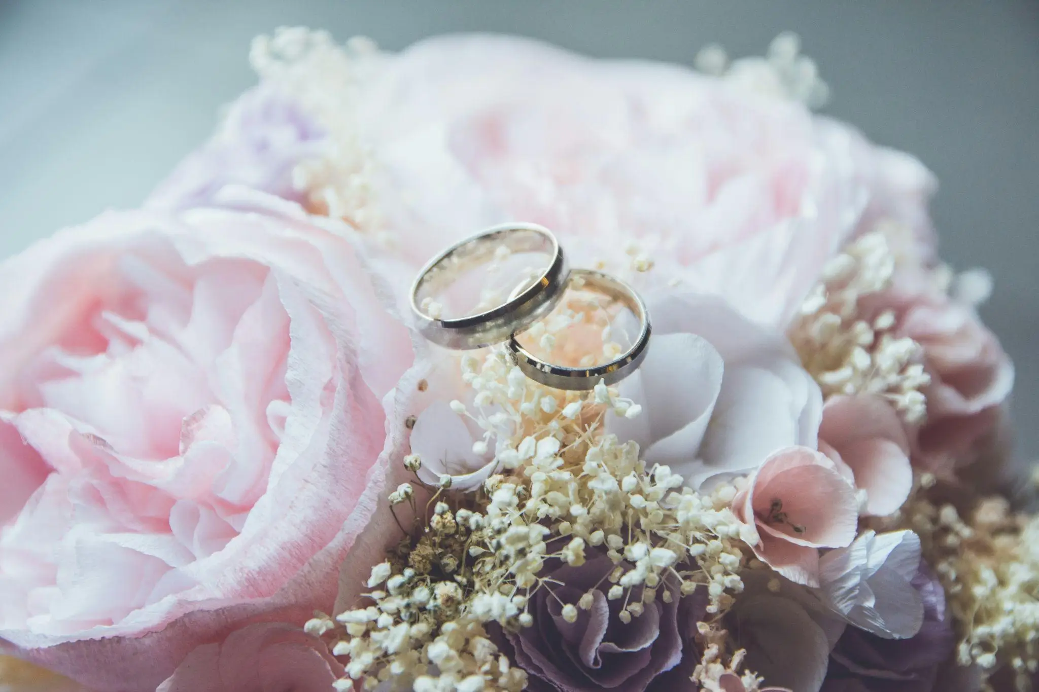Two silver wedding rings atop pastel pink and purple flower bouquet