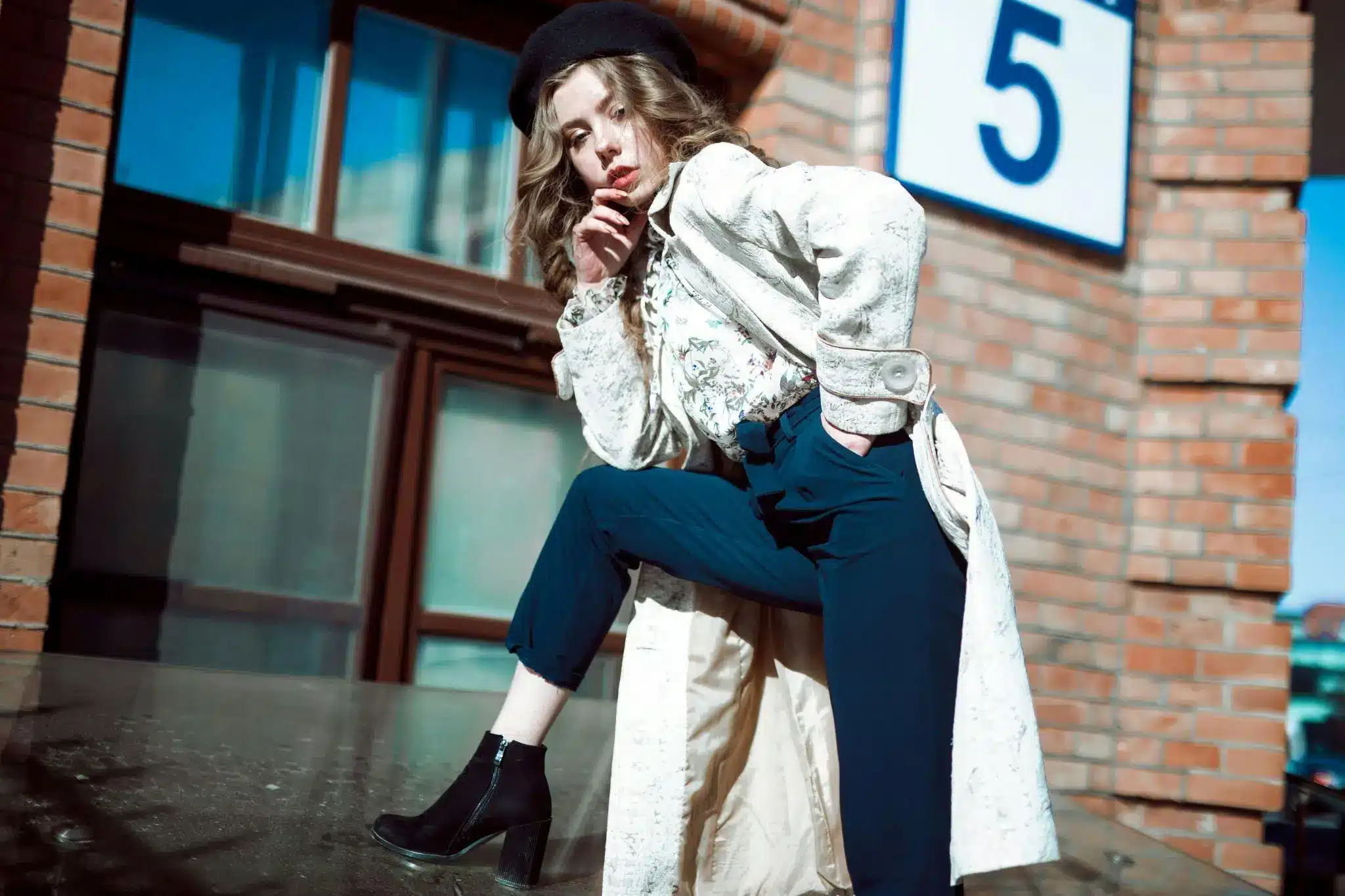 Person in stylish outfit posing against brick building background in bright sunlight