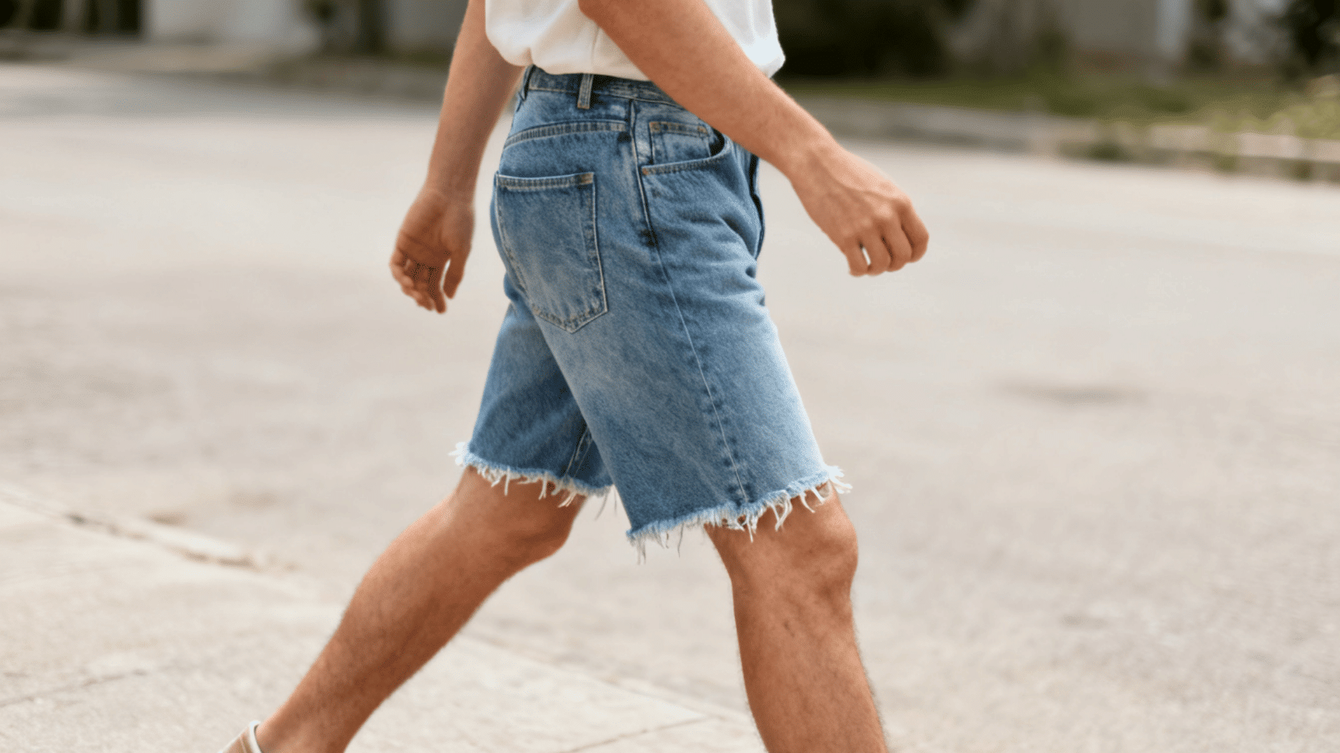 Person wearing blue cutoff jorts with raw frayed hems while walking outdoors.