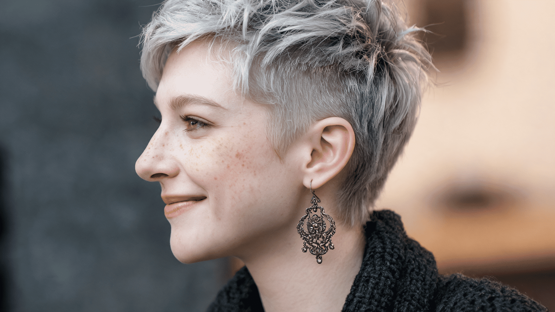 Person with asymmetrical textured pixie haircut wearing a white cable knit sweater in a close-up portrait
