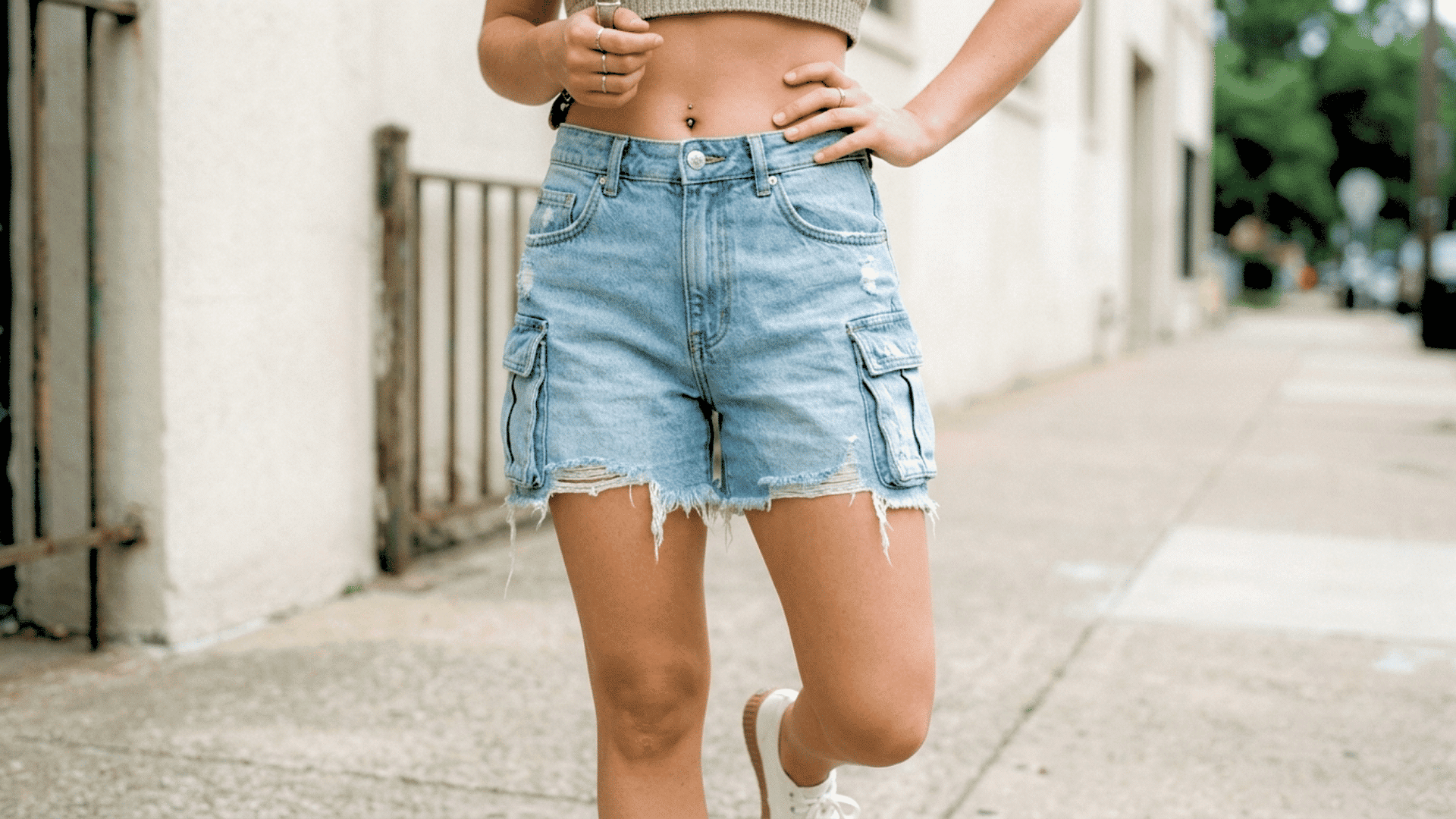 Person wearing high-waisted light blue jorts with frayed hems in an outdoor setting.