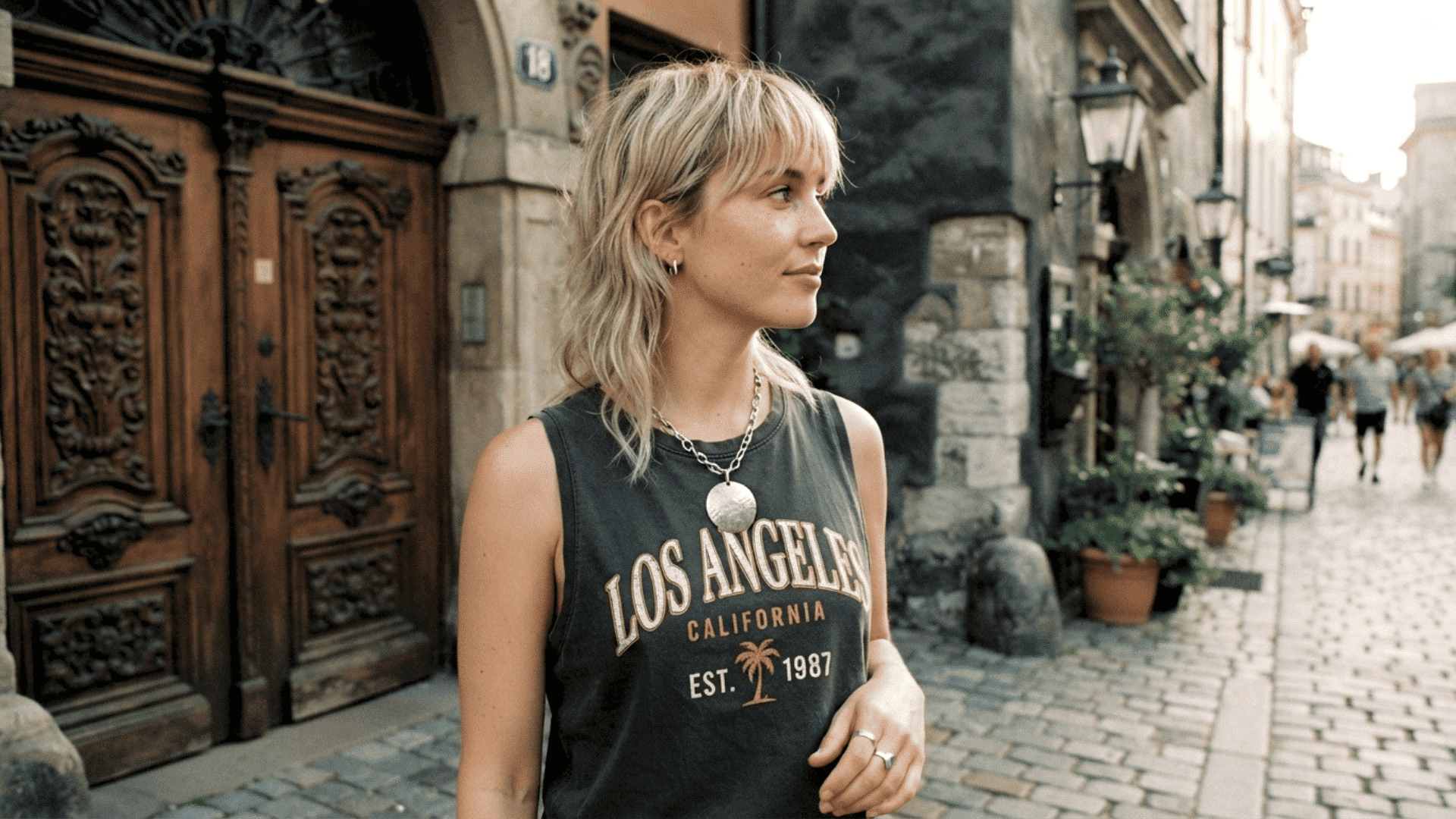 Person with blonde shag haircut wearing a sleeveless top while standing on a city street