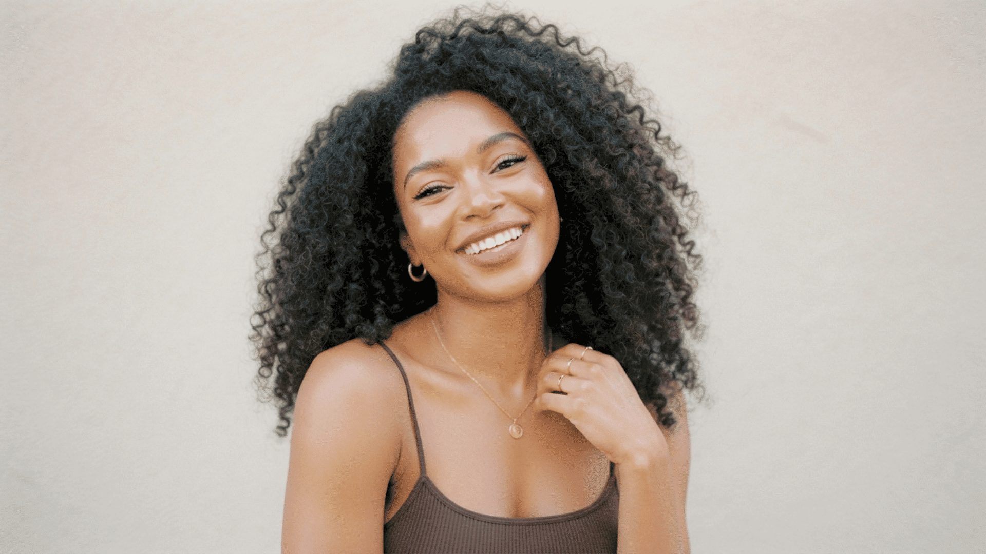 Person with natural curly afro hairstyle smiling in a portrait against a plain background