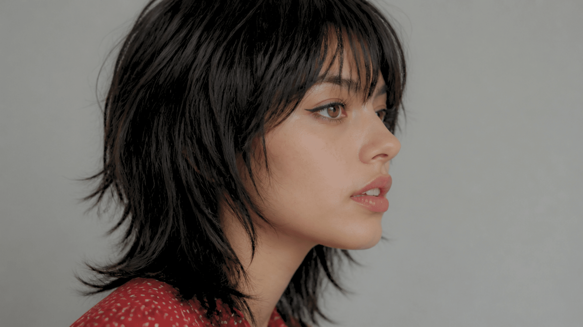 Person with black shag haircut and bangs posing in a side profile close-up portrait