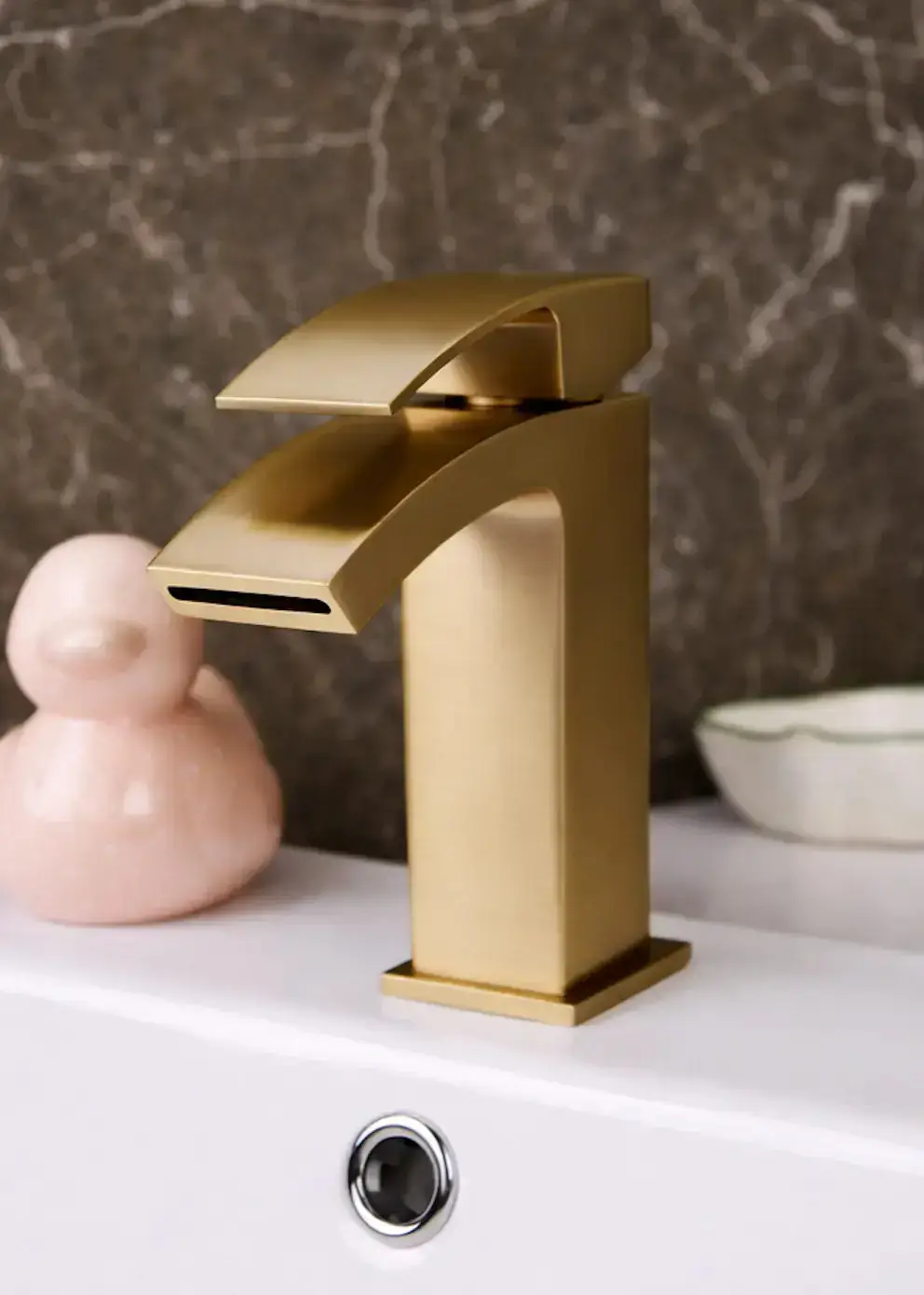 Modern gold faucet on white sink with gray marbled wall background