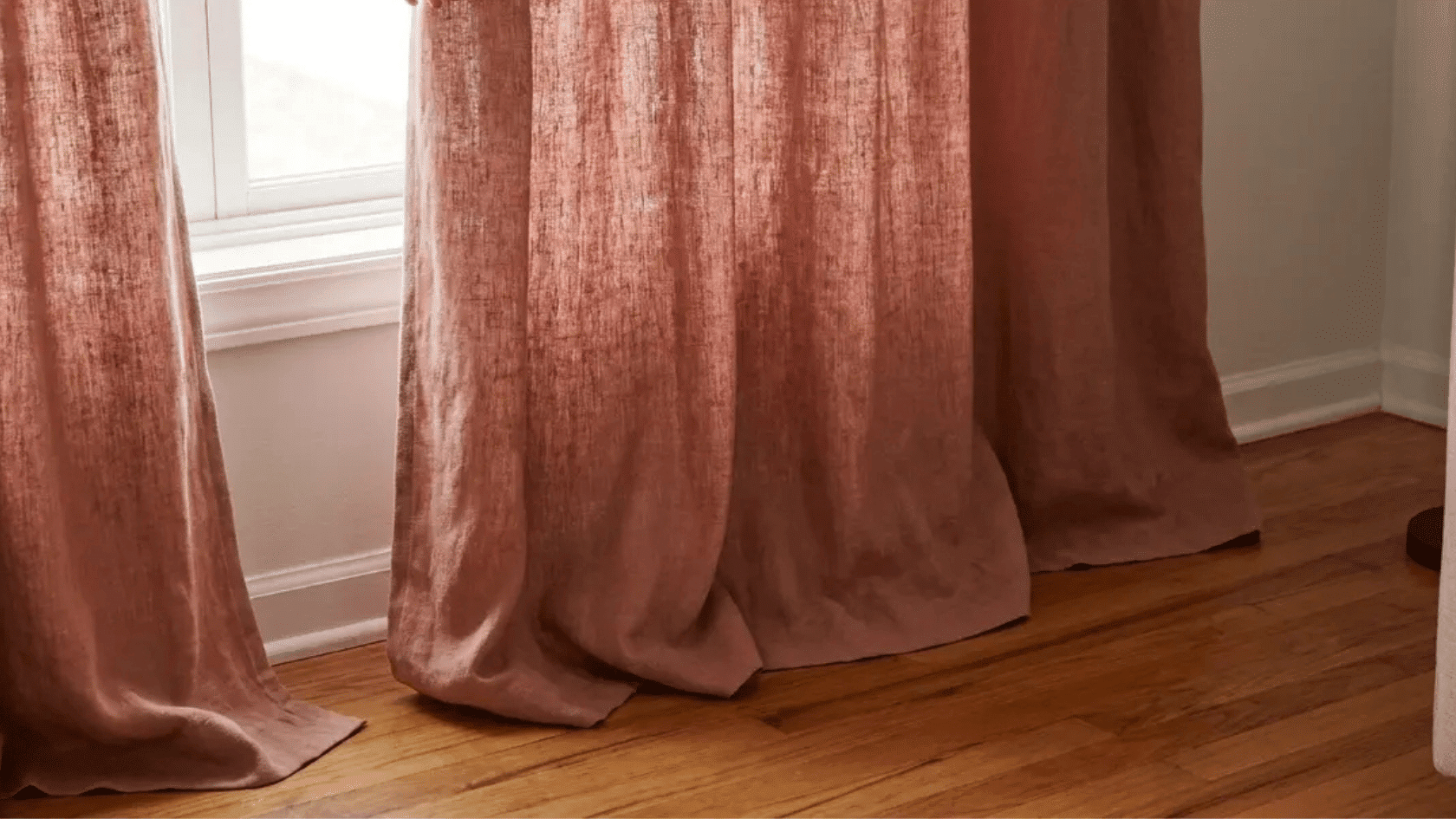 Pink floor-length curtains pooling slightly on a wooden floor in a cozy living room.