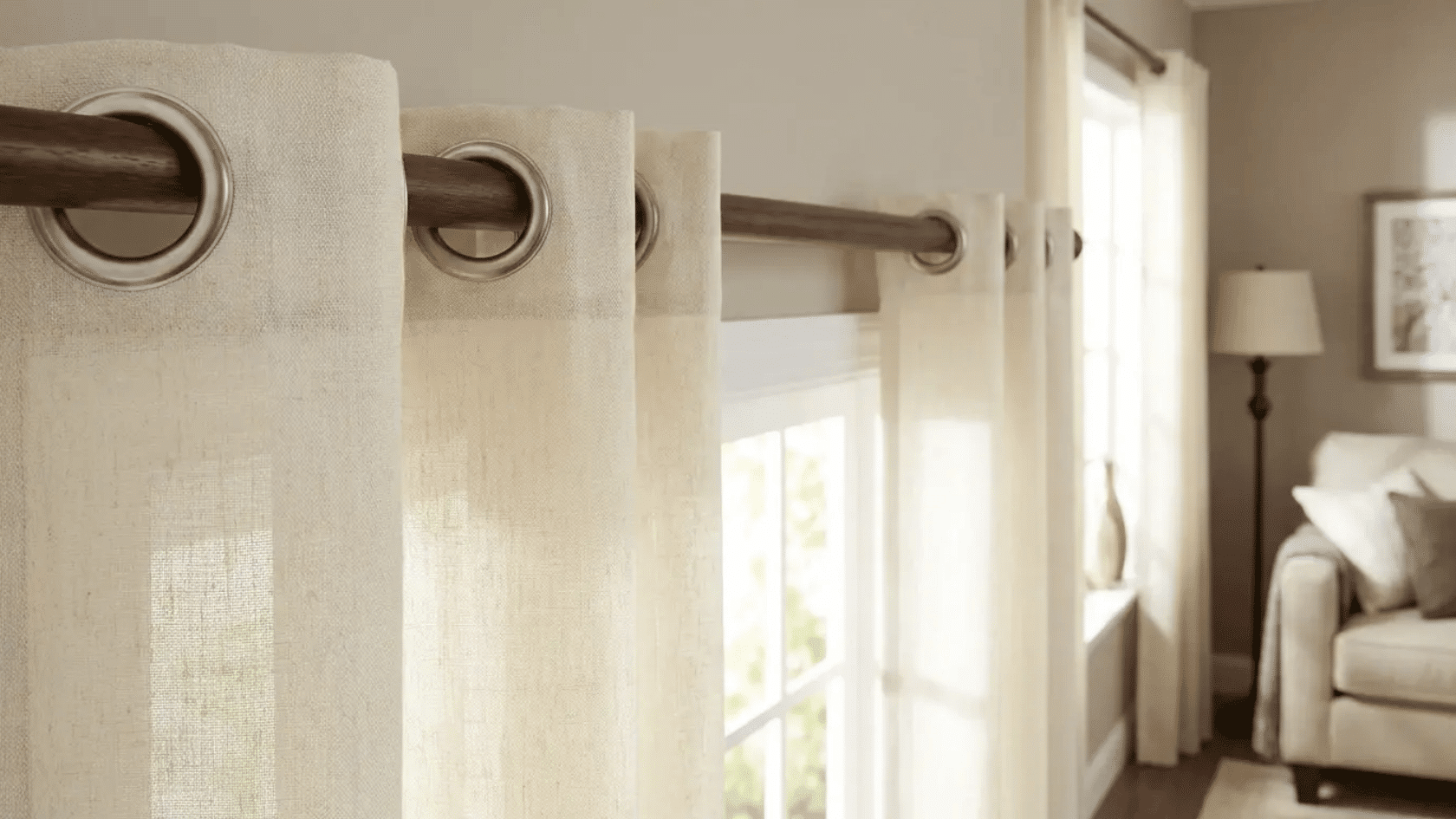 Cream grommet curtains hanging on a curtain rod, softly filtering natural light into a modern living room.