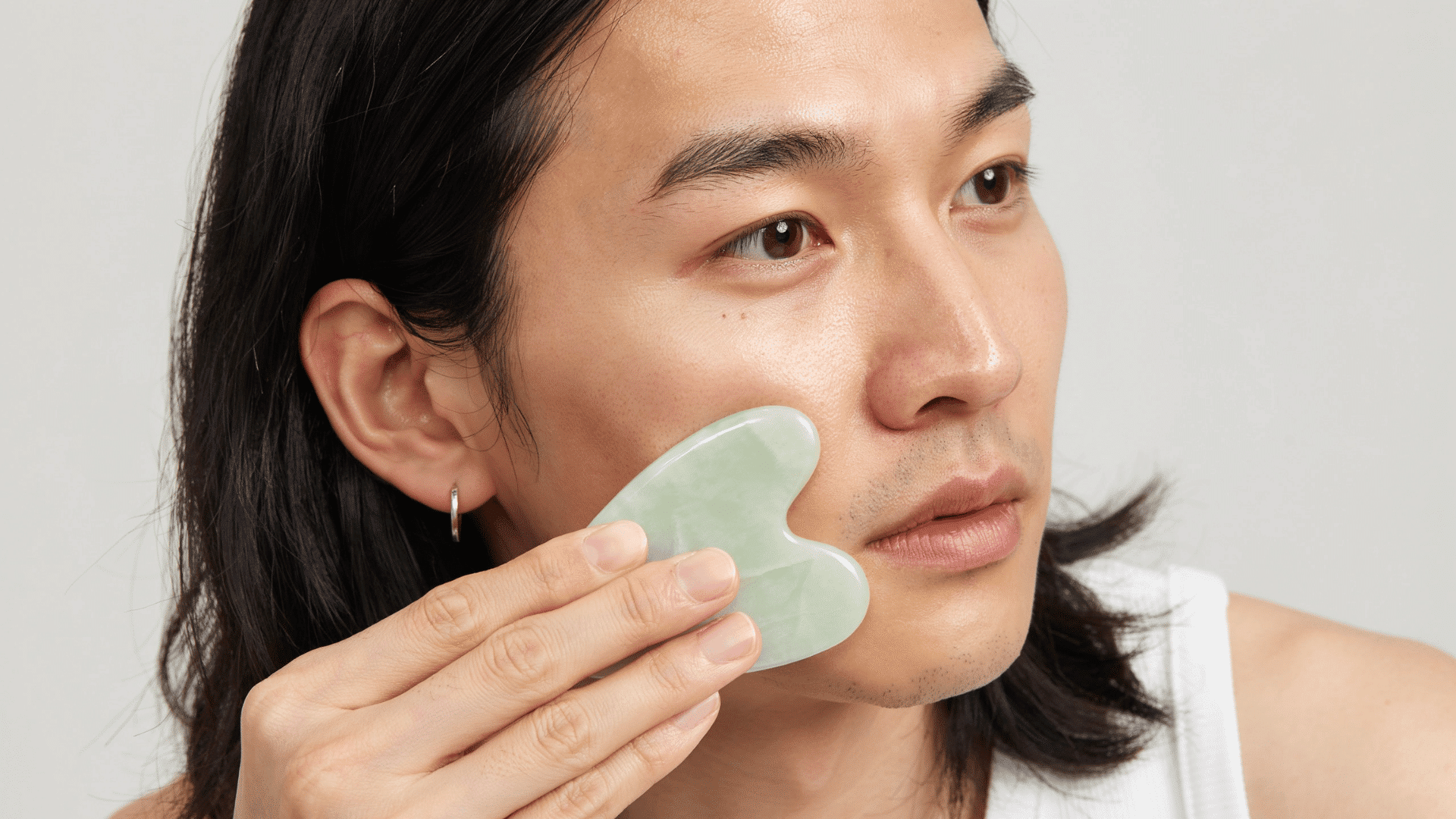 Person using gua sha tool for facial massage in a natural skin care routine at home
