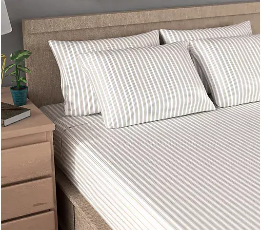 Striped bedding set on a beige upholstered bed with wooden nightstand and potted plant nearby