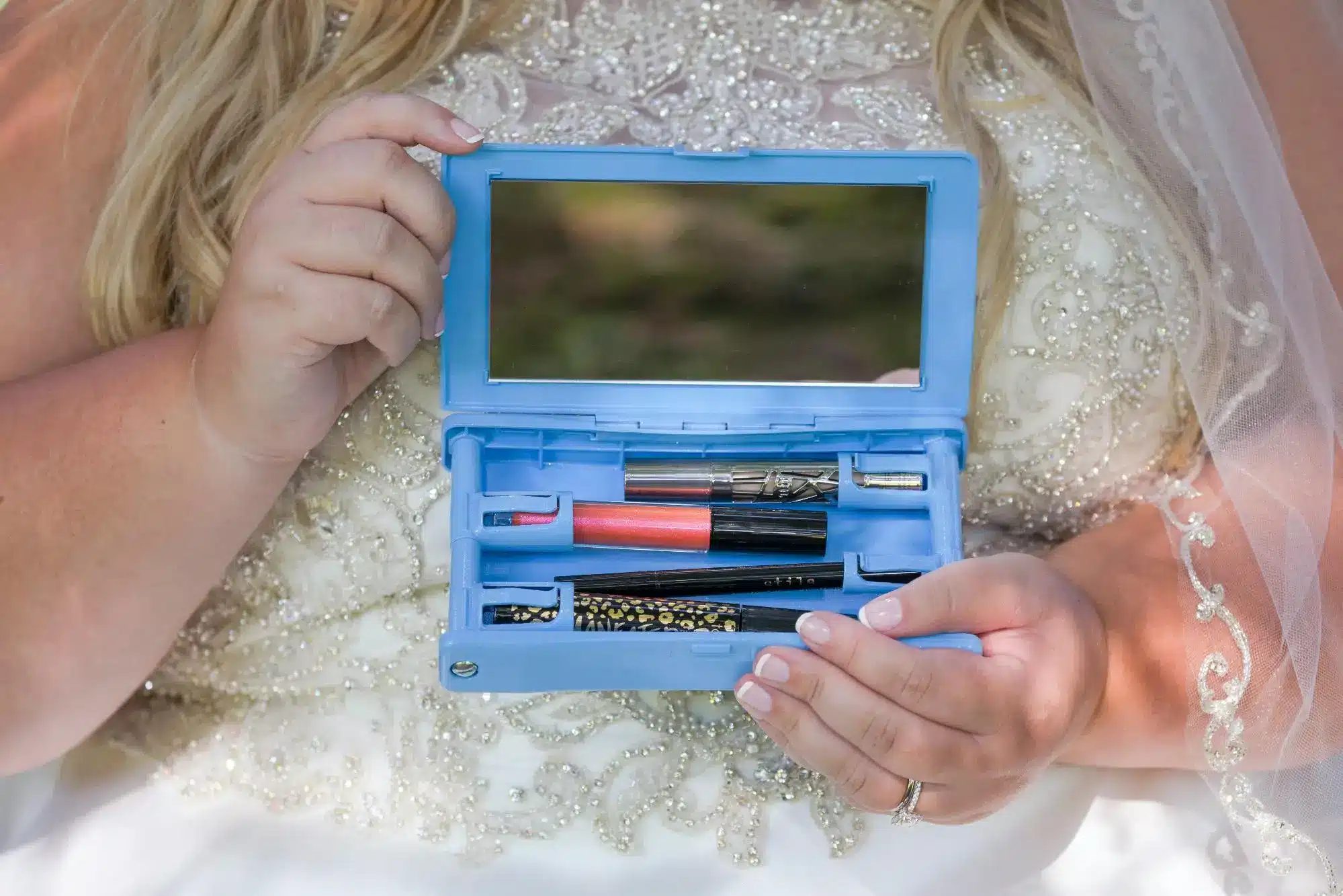 Bride holding blue makeup kit with lipstick and mascara in ornate wedding dress