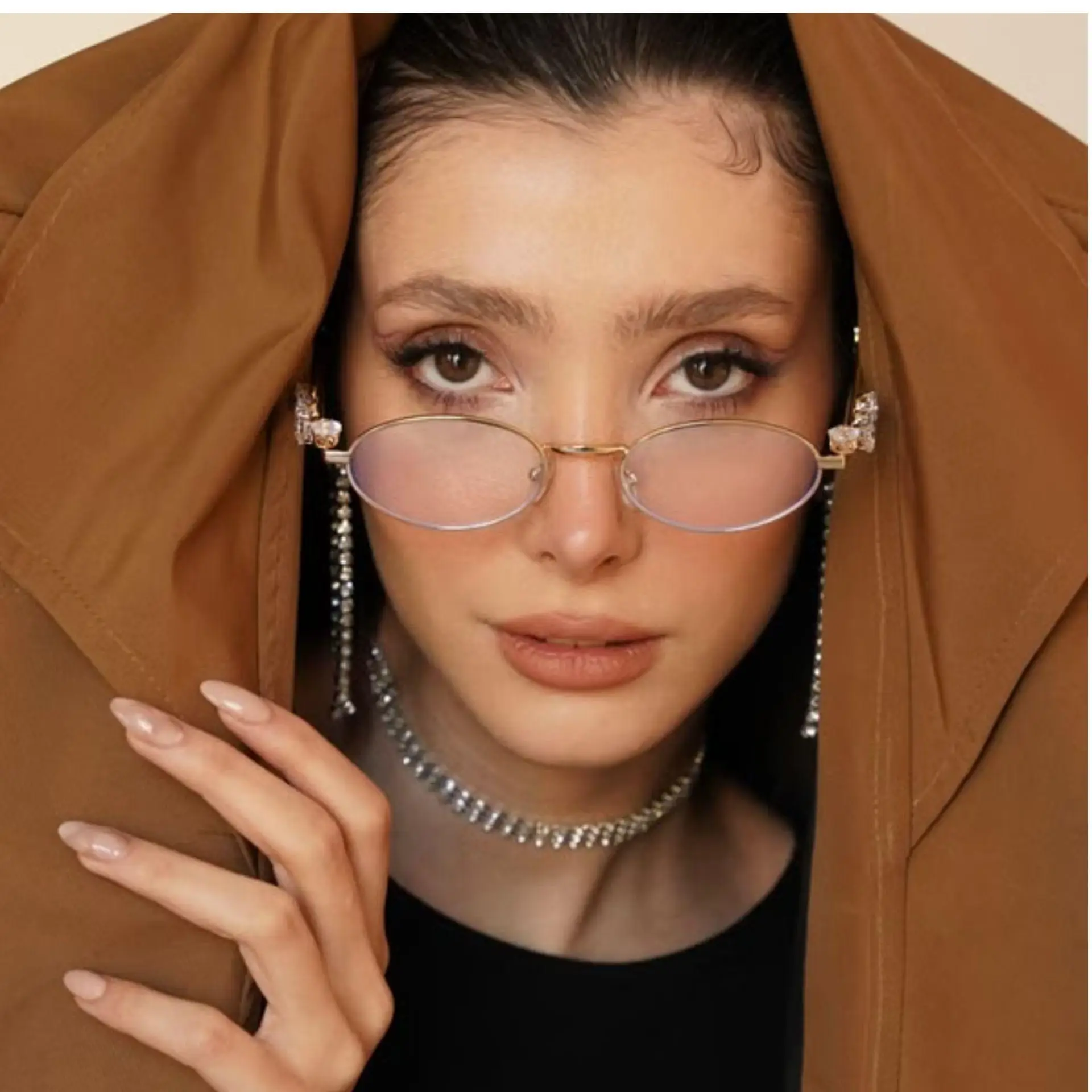 Woman wearing vintage glasses under brown coat with elegant jewelry and manicure