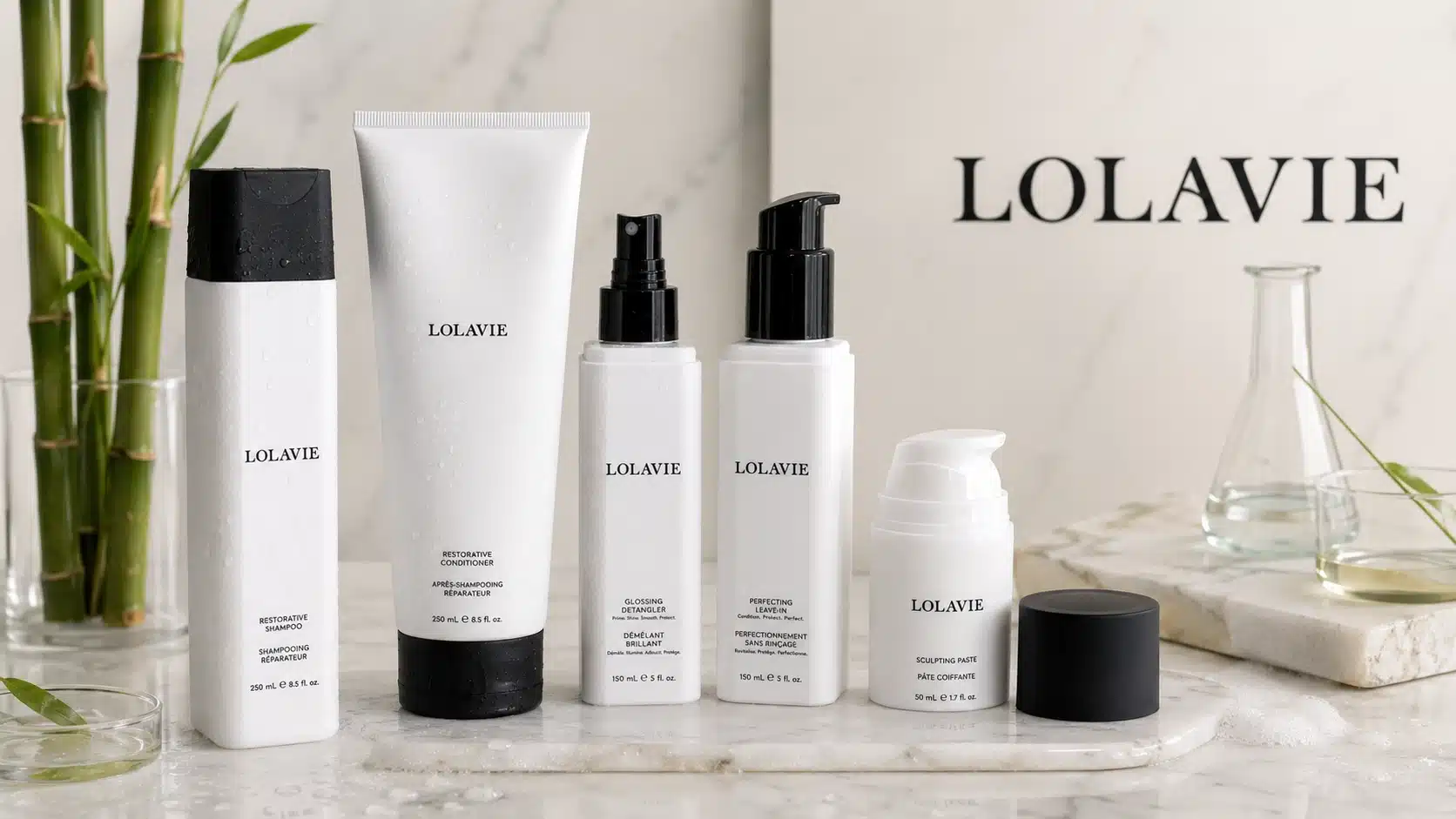 White hair care products displayed on a marble surface with bamboo and glass accents.