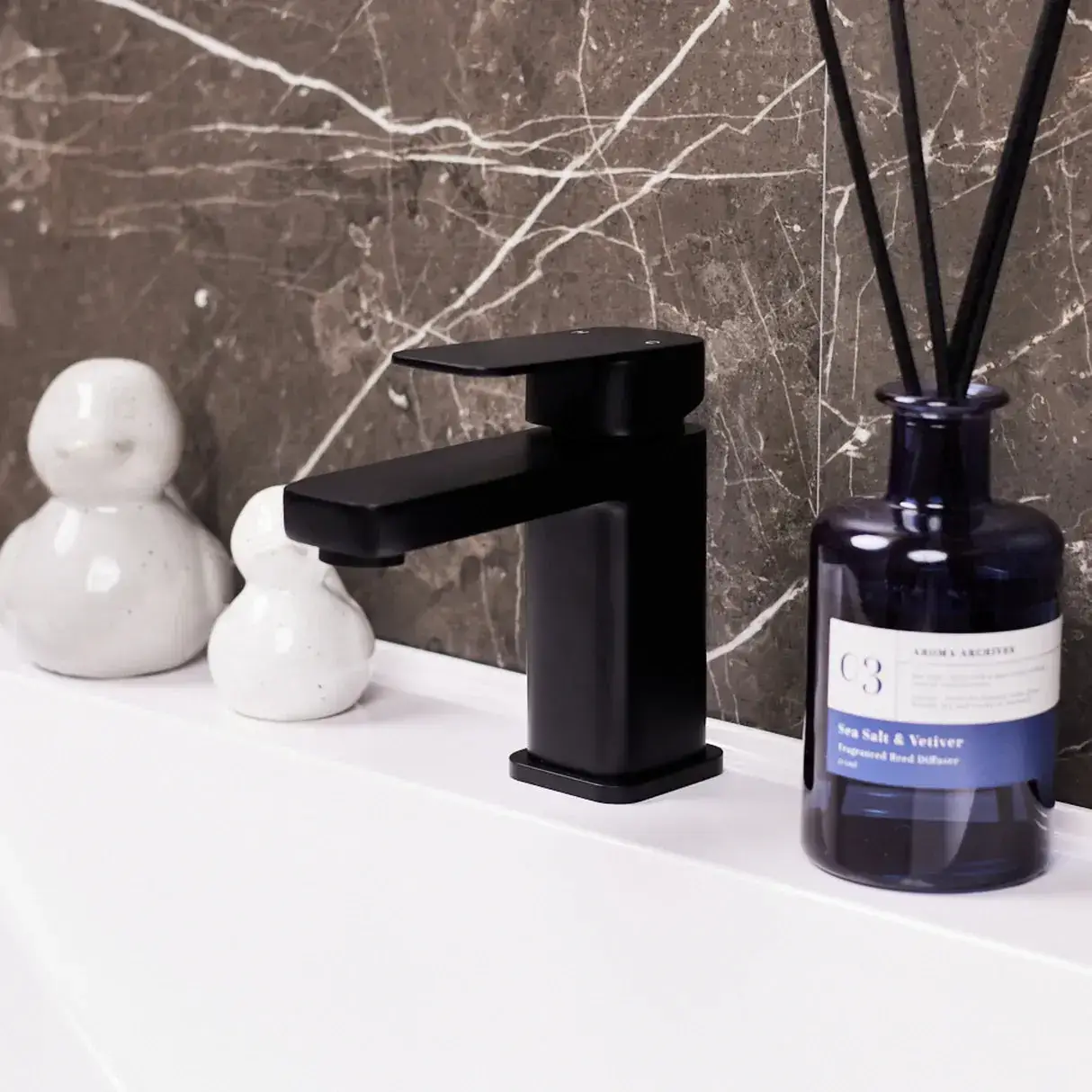 Black faucet on white sink with marble backsplash and blue fragrance bottle