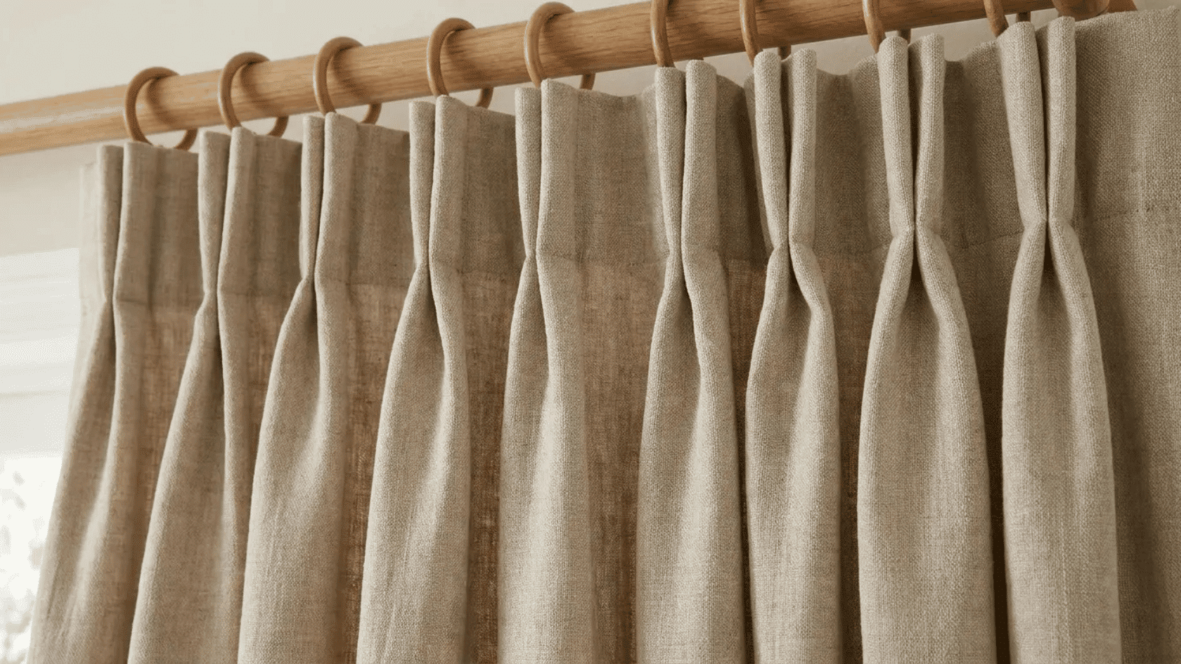 Beige pencil pleat curtains with gathered folds hanging from a wooden curtain rod