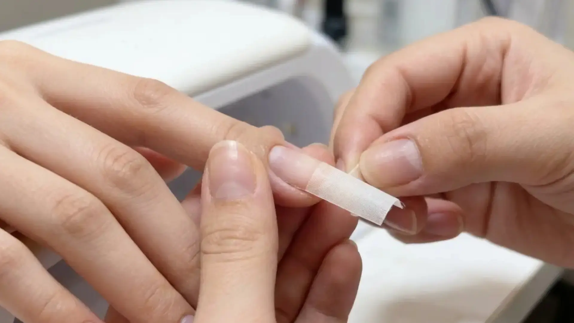 person applying small adhesive strip to another person’s fingernail during a manicure process
