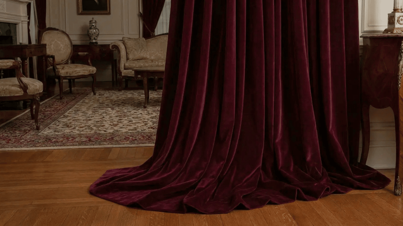 Deep burgundy puddle curtains draping onto a wooden floor in an elegant formal room.
