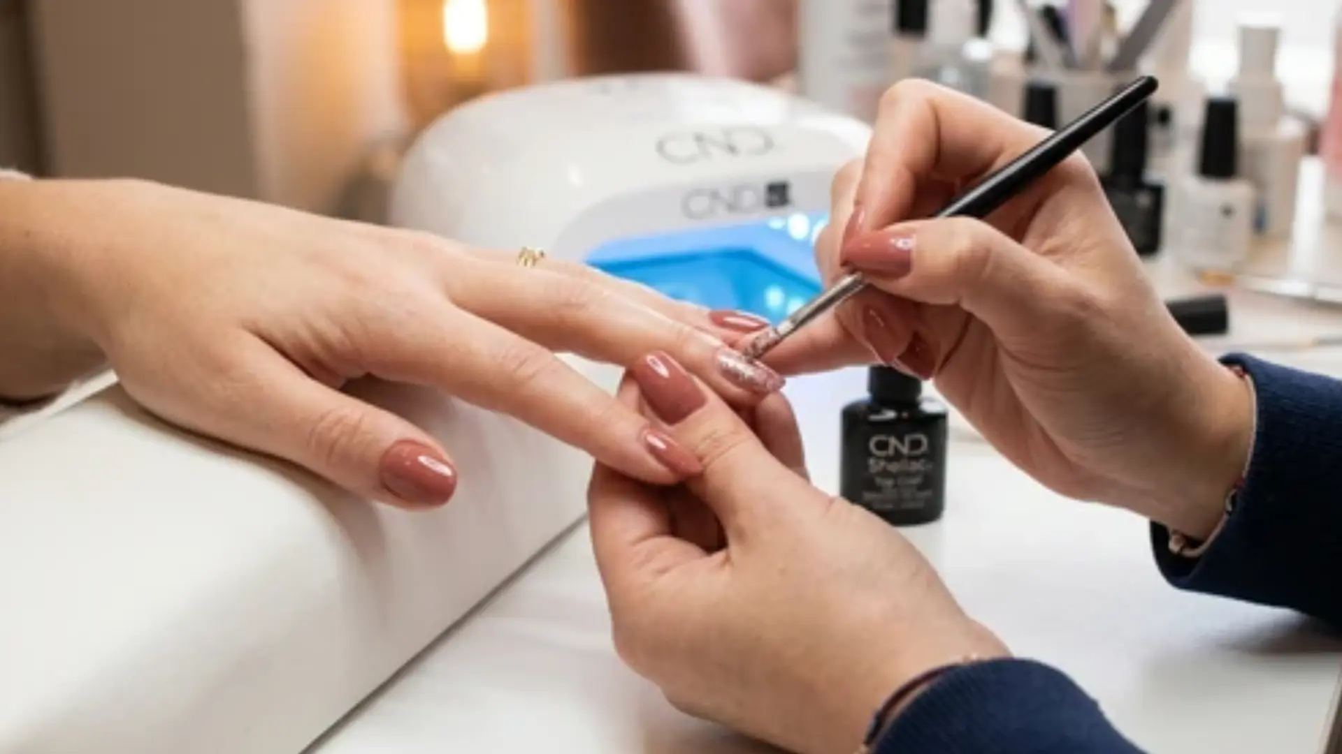 shellac nails with the glitter applying tool in the technician's hand