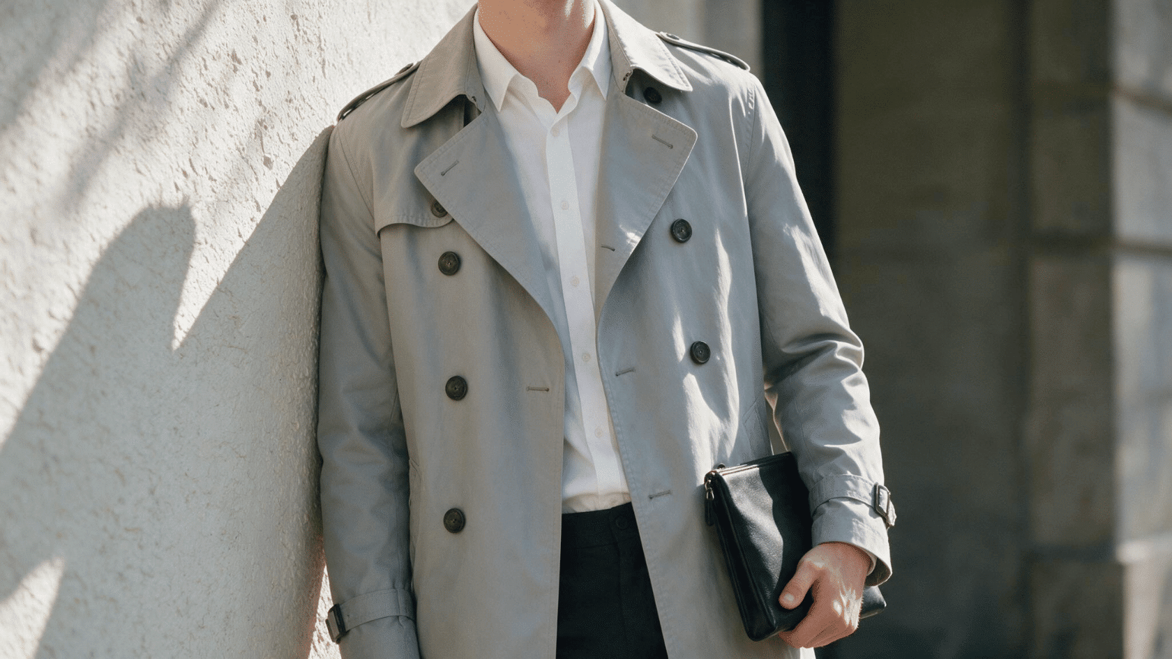 Person wearing a light-colored trench coat with double-breasted buttons and shoulder straps.