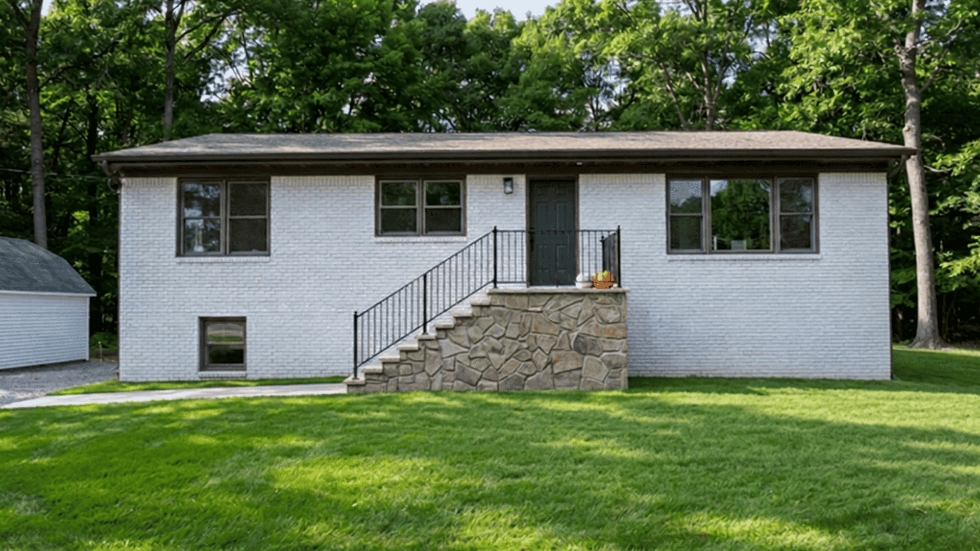 White house exterior with black trim, stone staircase, lawn, and surrounding trees