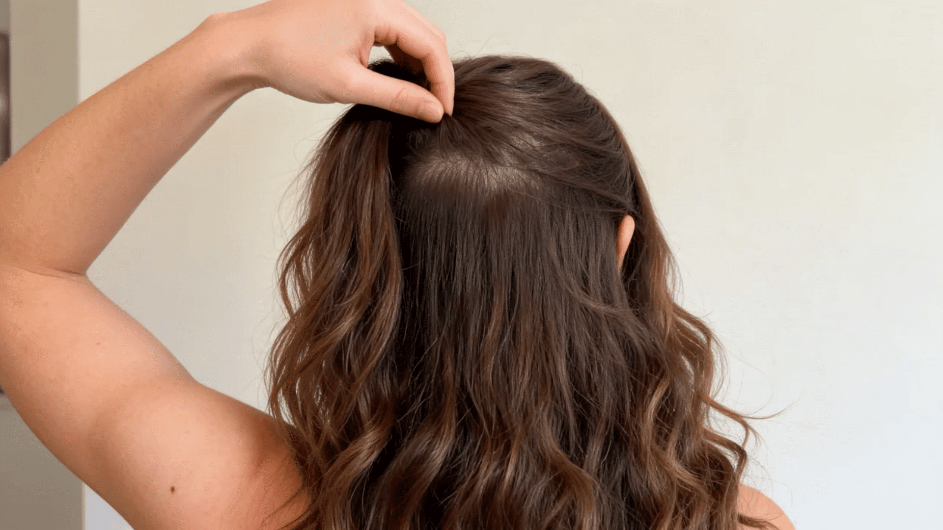 Woman lifting her top hair to compare a straighter crown with curlier sections near the nape.