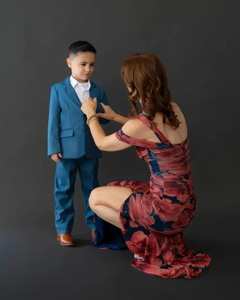 Woman adjusting a young boy's blue suit jacket in a formal studio setting