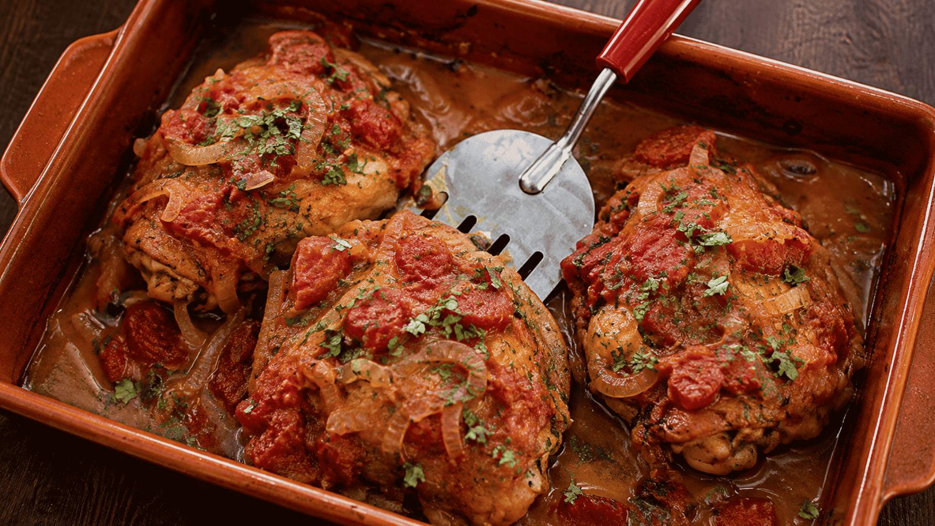baked chicken with tomato onion sauce and fresh herbs in a rustic ceramic dish